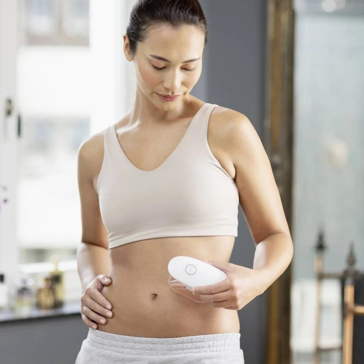 Femme en soutien-gorge tenant un dispositif médical blanc sur son abdomen.