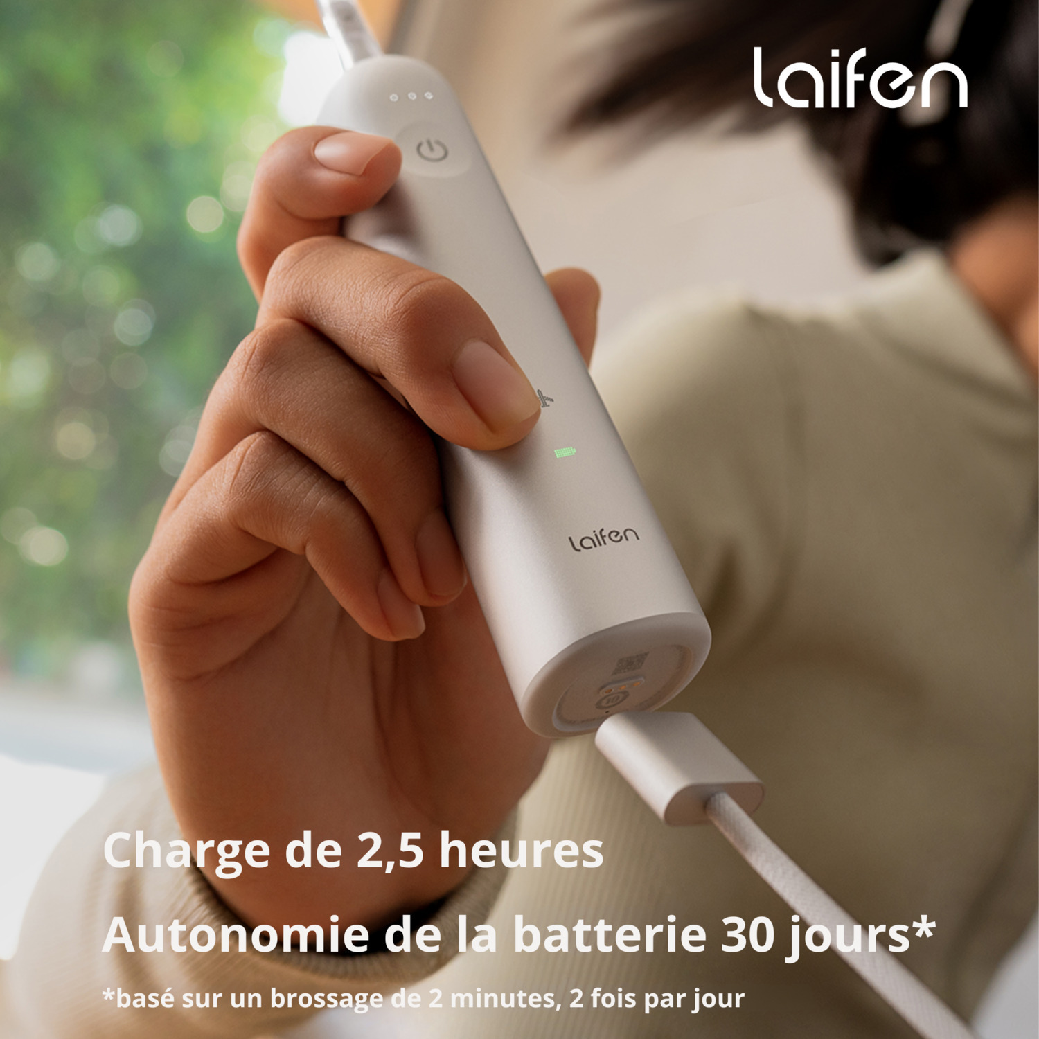 Personne tenant une brosse à dents électrique blanche avec texte: 2,5 heures de charge, 30 jours de batterie.