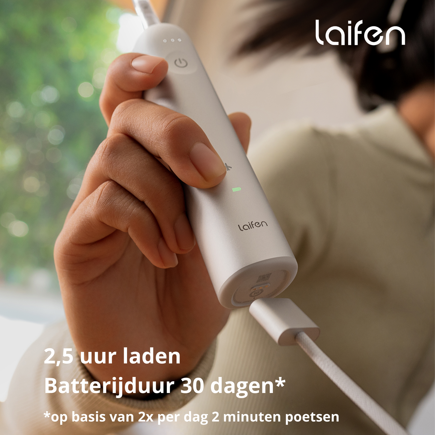 Persoon houdt een witte elektrische tandenborstel vast, die oplaadt met een kabel.