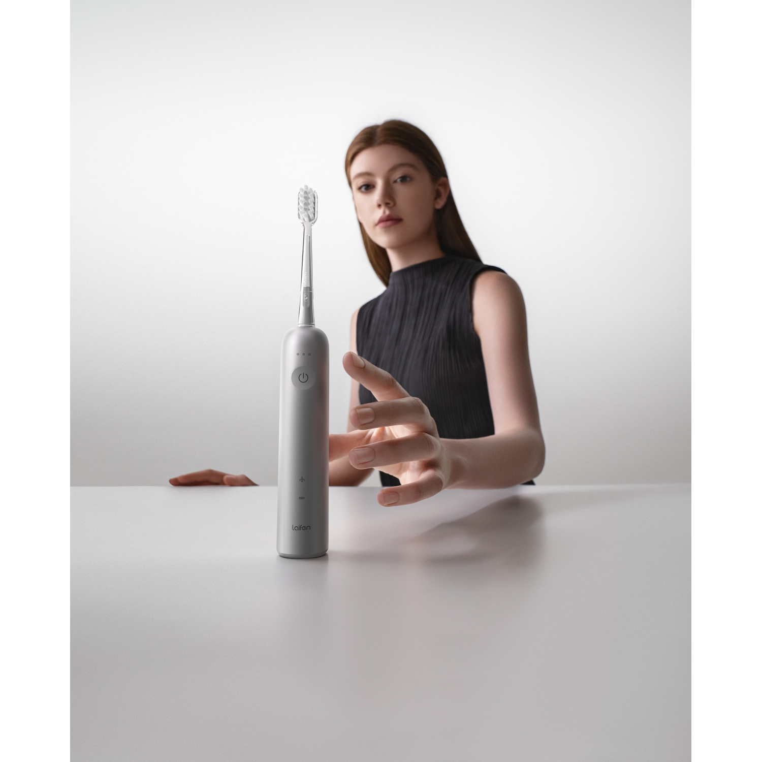 Femme tenant une brosse à dents électrique argentée sur une table blanche.
