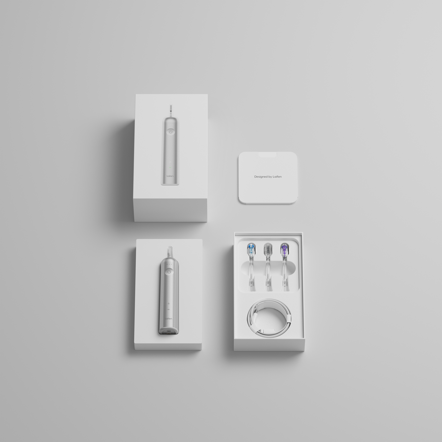 Boîtes blanches contenant brosse à dents, socle de charge et têtes sur surface grise. Vue de dessus.