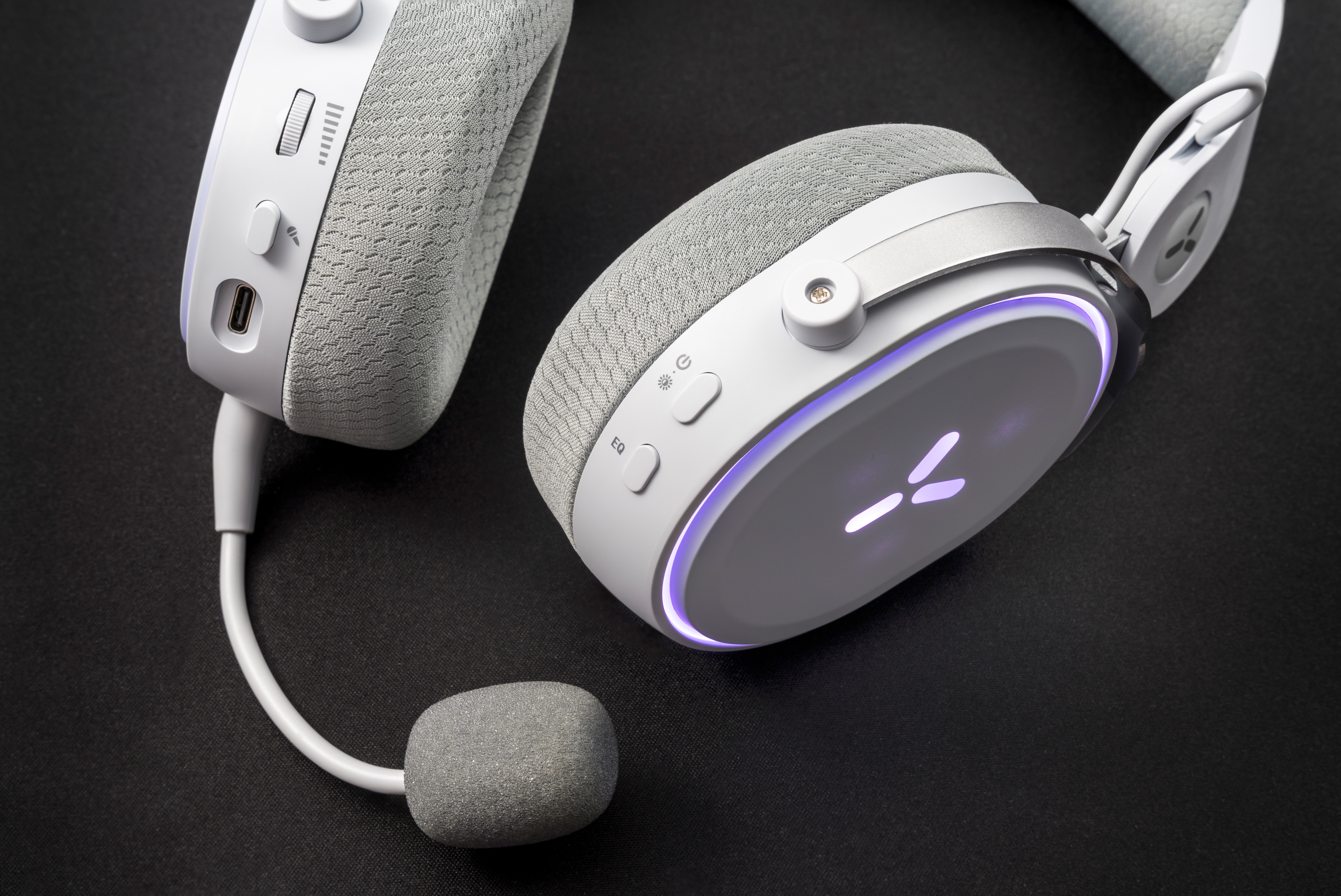 Białe słuchawki z mikrofonem. Zawiera regulację głośności i przycisk zasilania. Czarne tło.