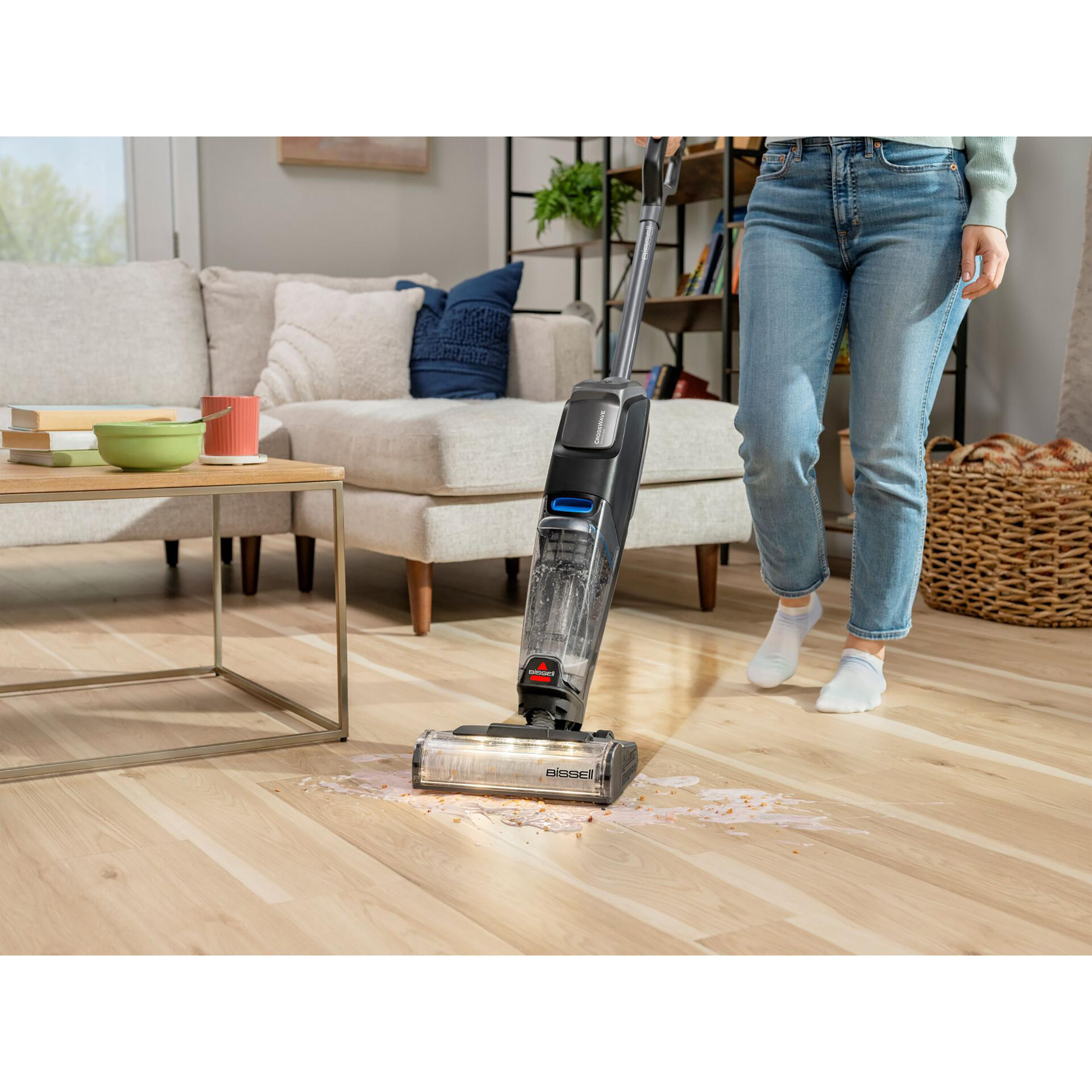 Person saugt einen Holzboden, mit verschütteter Flüssigkeit auf dem Boden.
