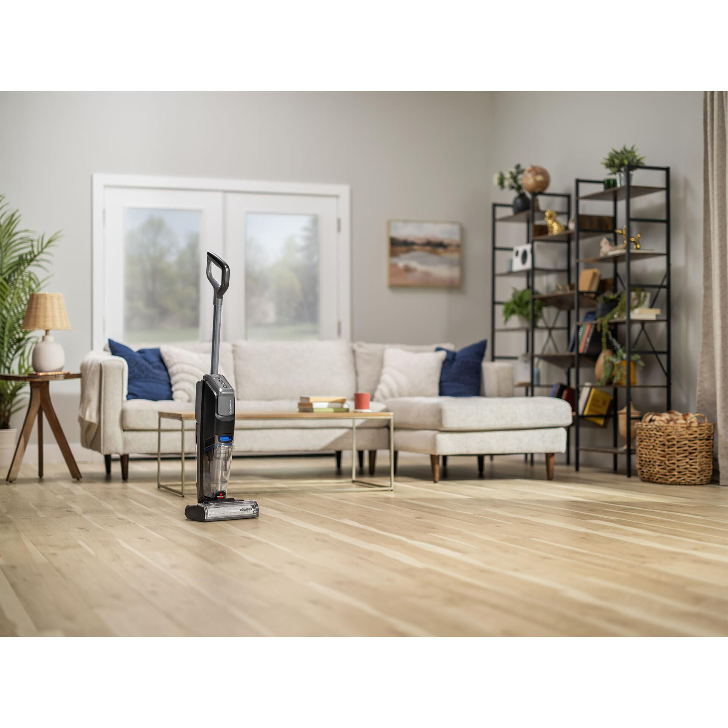 Ein Staubsauger in einem Wohnzimmer. Das Zimmer hat Holzböden, ein Sofa und ein Bücherregal.