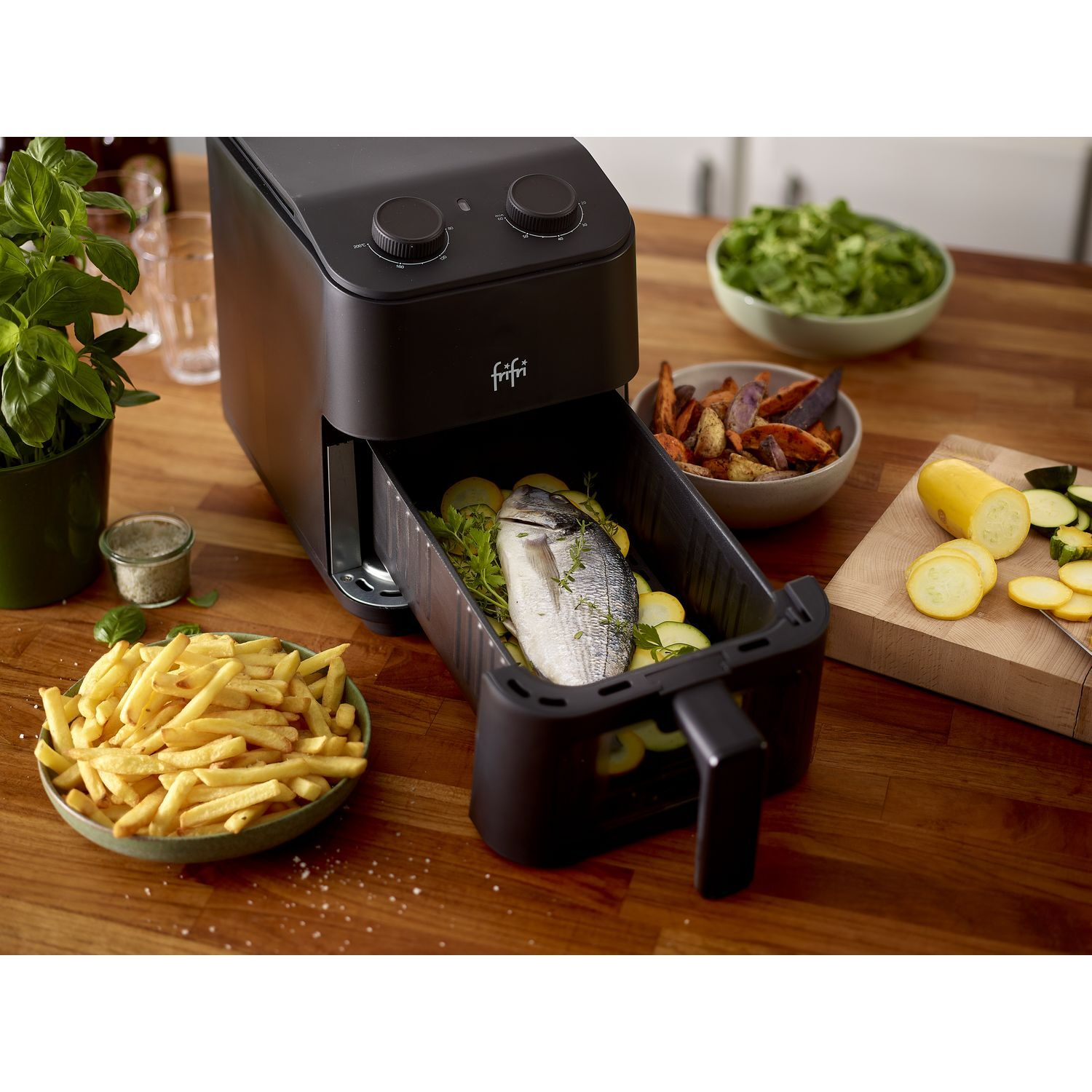 Airfryer met eten erin, groenten en friet eromheen.