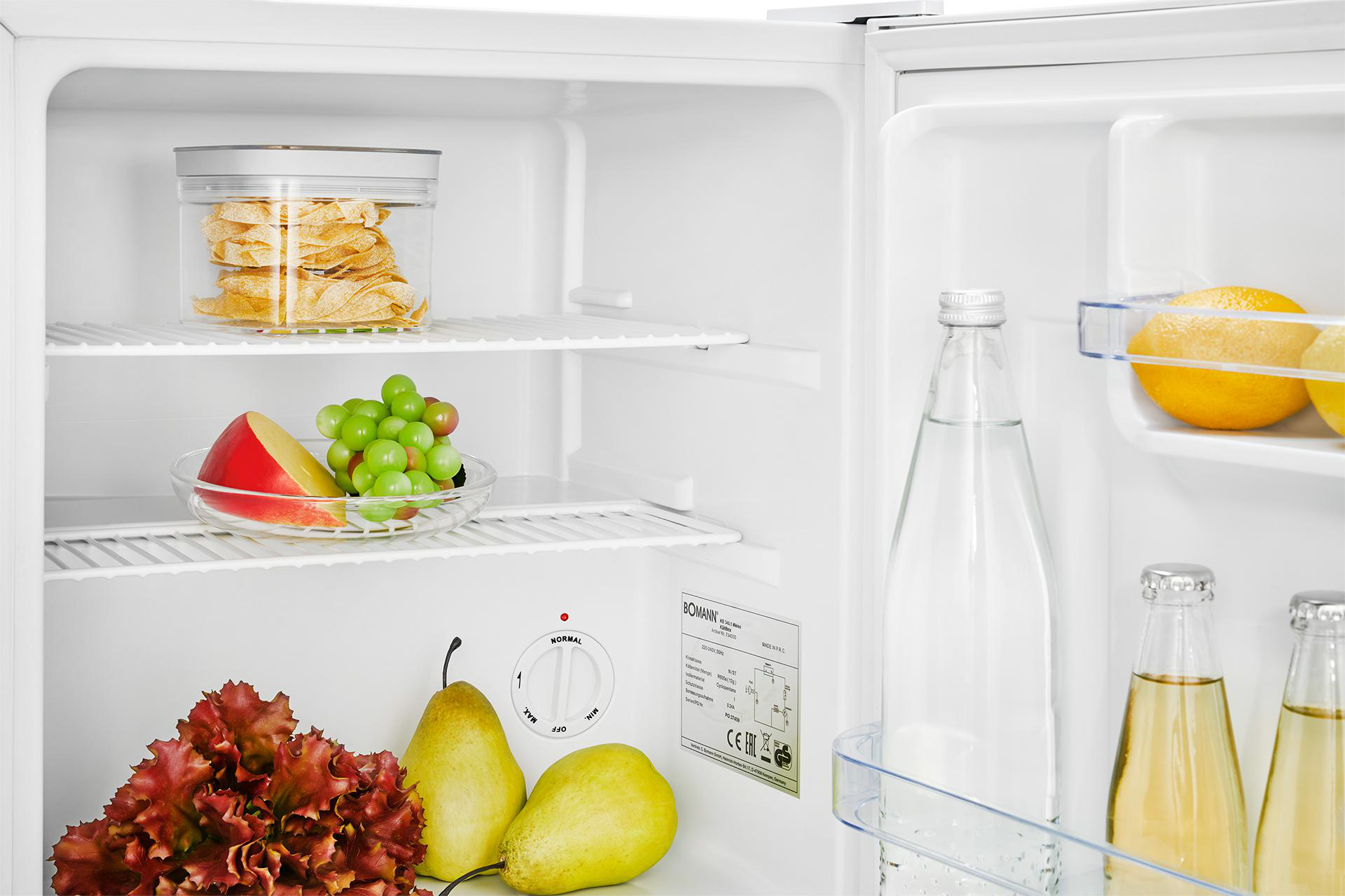 Kühlschrankinneres mit Lebensmitteln: Glasbehälter mit Keksen, Obst, Gemüse und Flaschen.