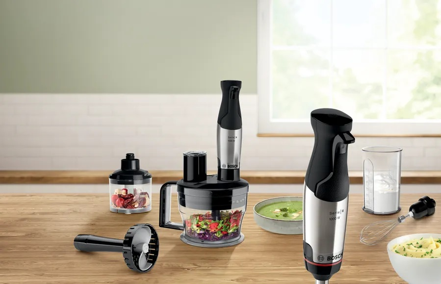 Blender z akcesoriami i składnikami na drewnianym stole.