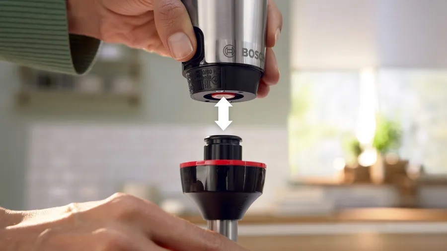 Osoba podłączająca srebrną przystawkę blendera Bosch, ze strzałką w dół.