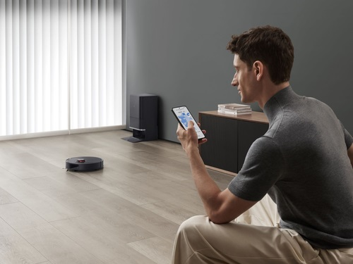 Mężczyzna używa smartfona do sterowania robotem sprzątającym na drewnianej podłodze.