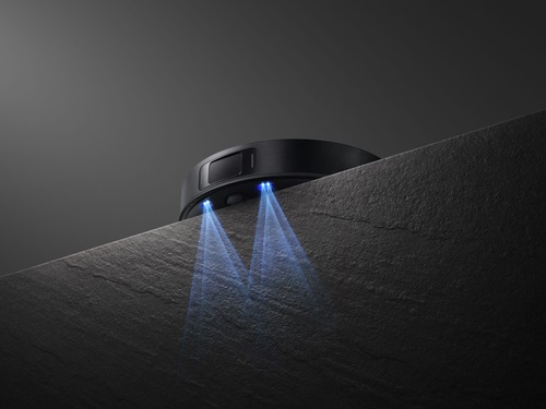 Czarne urządzenie na powierzchni, emitujące dwie niebieskie wiązki światła, na ciemnoszarej powierzchni.