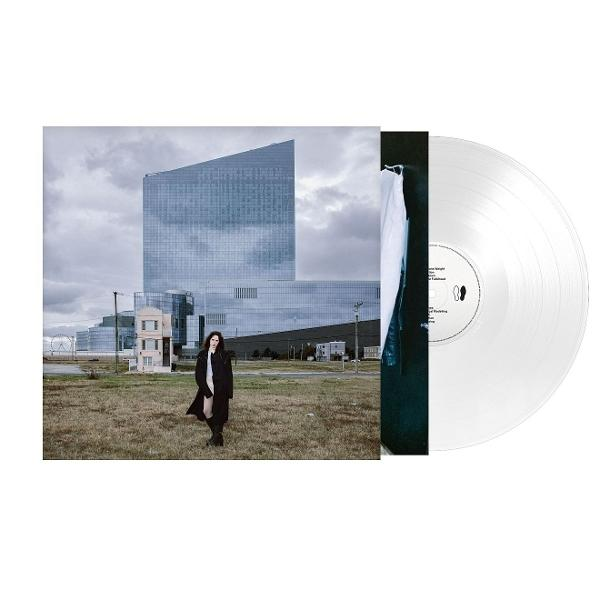 Frau in schwarzem Mantel vor modernem Gebäude, Vinyl-Schallplatte rechts. Bewölkter Himmel.