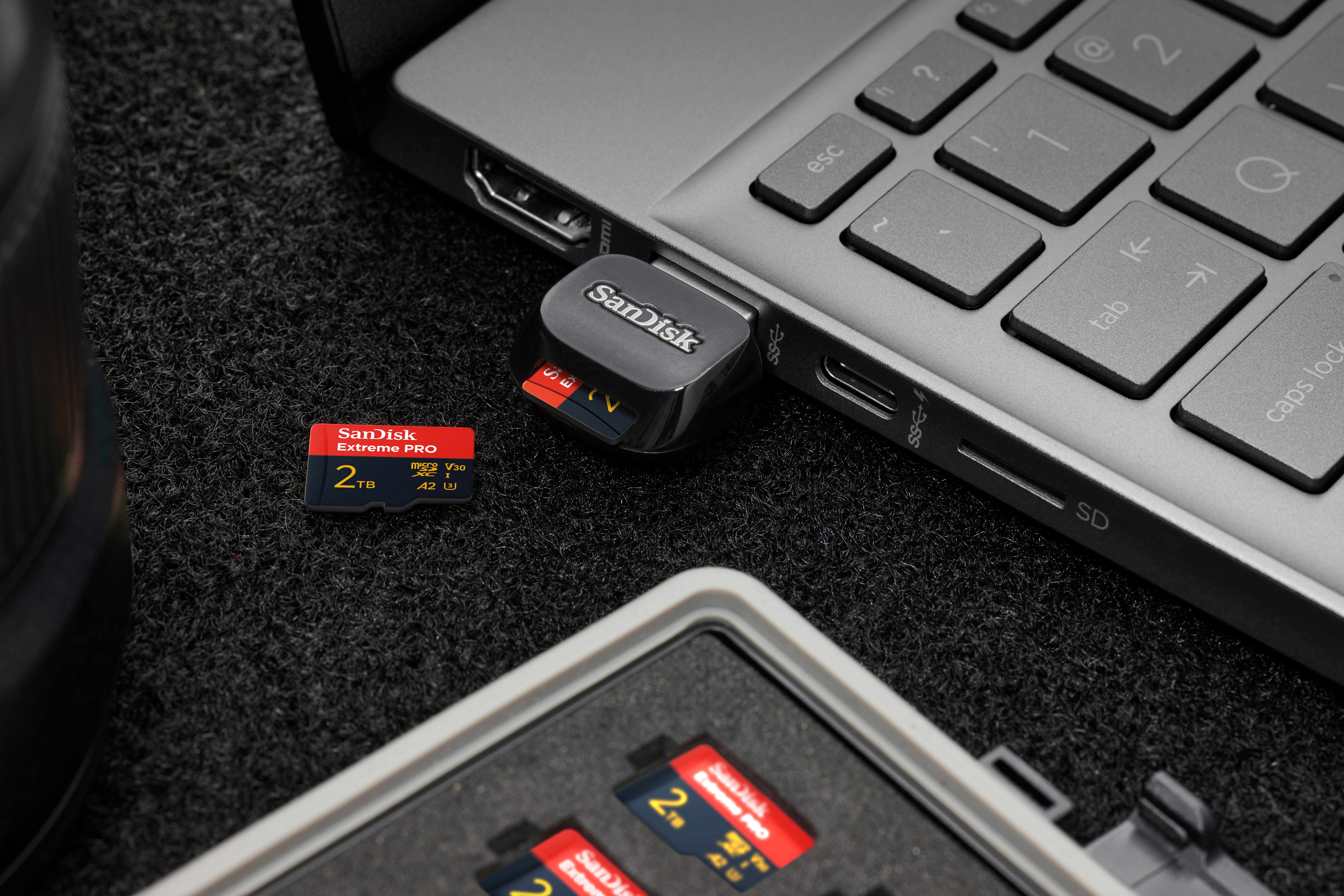 Ein Sandisk USB-Laufwerk und ein Speicherkartenleser neben einem Laptop. Mehrere Speicherkarten vorhanden.