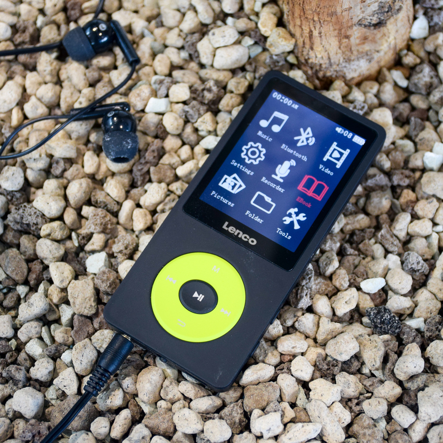 Black MP3 player with green controls, earphone, and cord on a bed of stones.