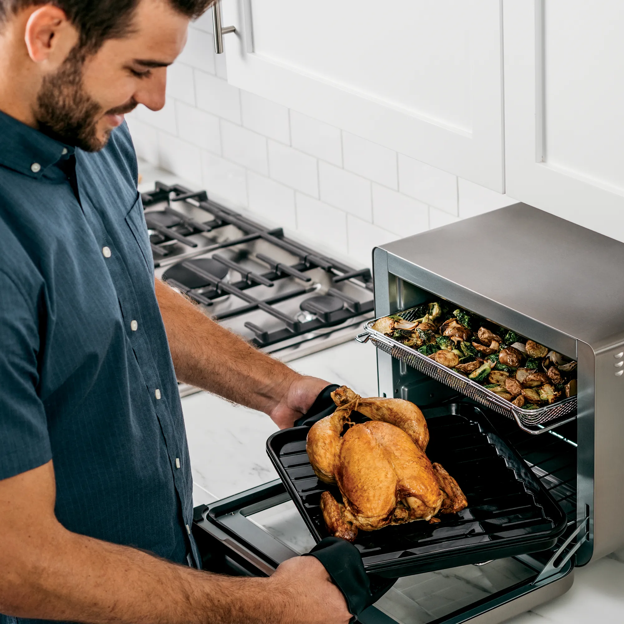 Un uomo che mette un pollo cotto sulla griglia dentro un forno.