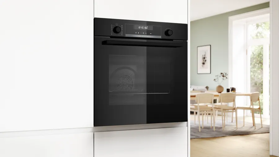 Forno nero incassato in armadi bianchi. Sala da pranzo sullo sfondo.