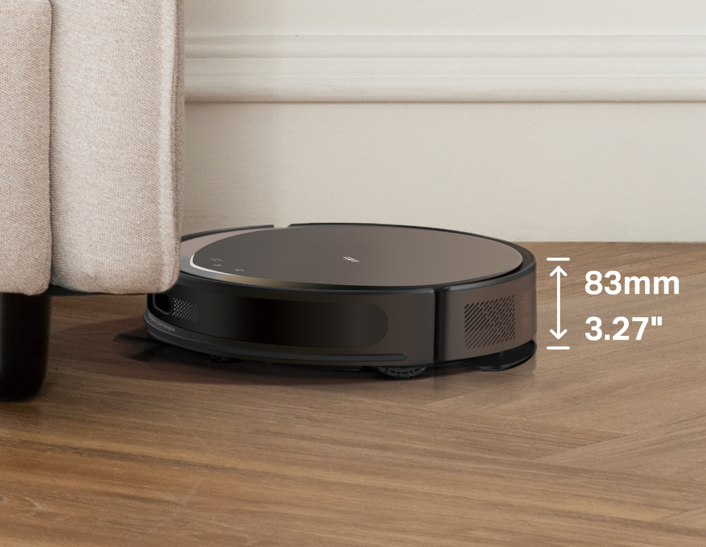 Egy fekete robotporszívó tisztítja a fa padlót egy bézs kanapé közelében.