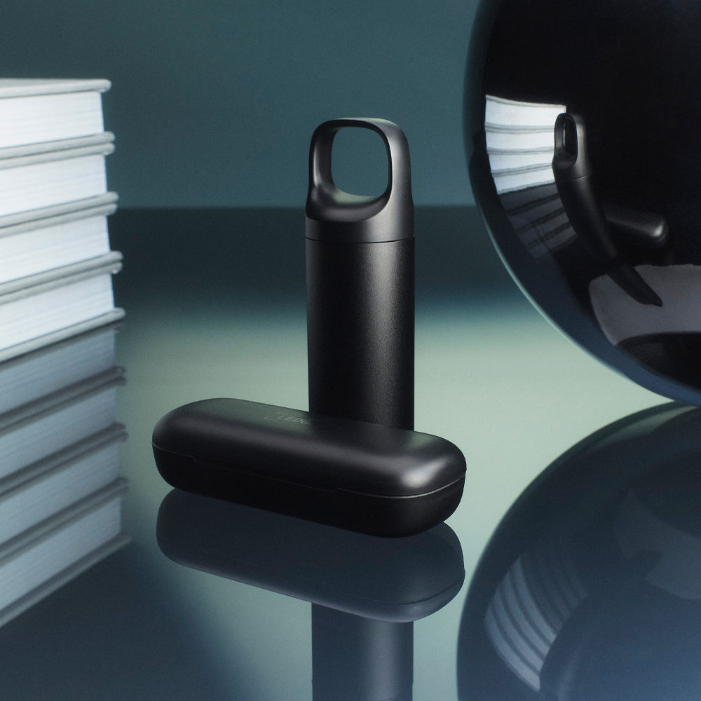 Schwarze zylindrische Objekte, eines mit Schlaufe, auf reflektierender Oberfläche.