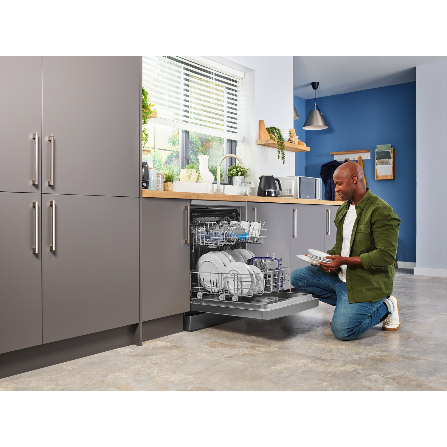 Uomo che carica una lavastoviglie con piatti in una cucina moderna.