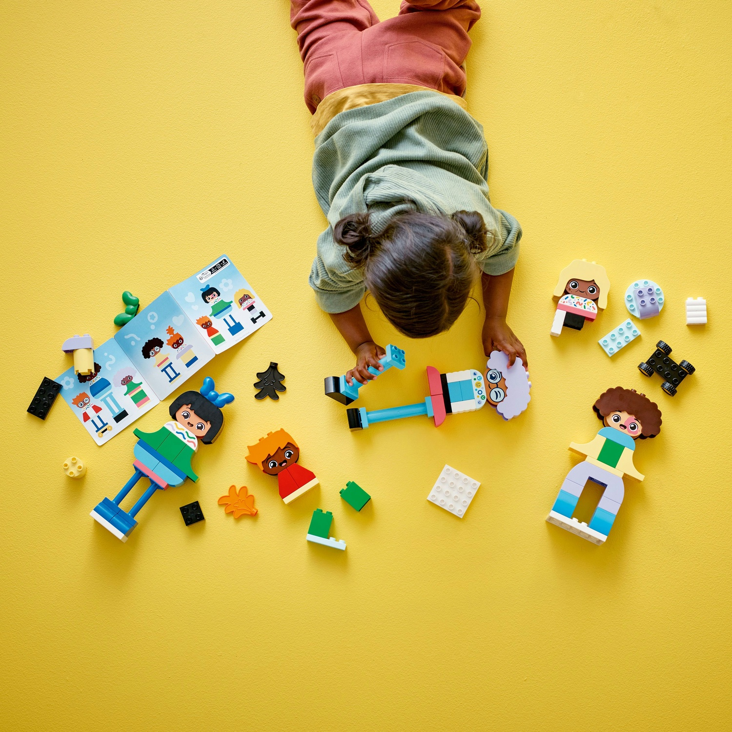 Un bambino gioca con i mattoncini LEGO Duplo su una superficie gialla. Diverse figure e mattoncini sono sparsi.