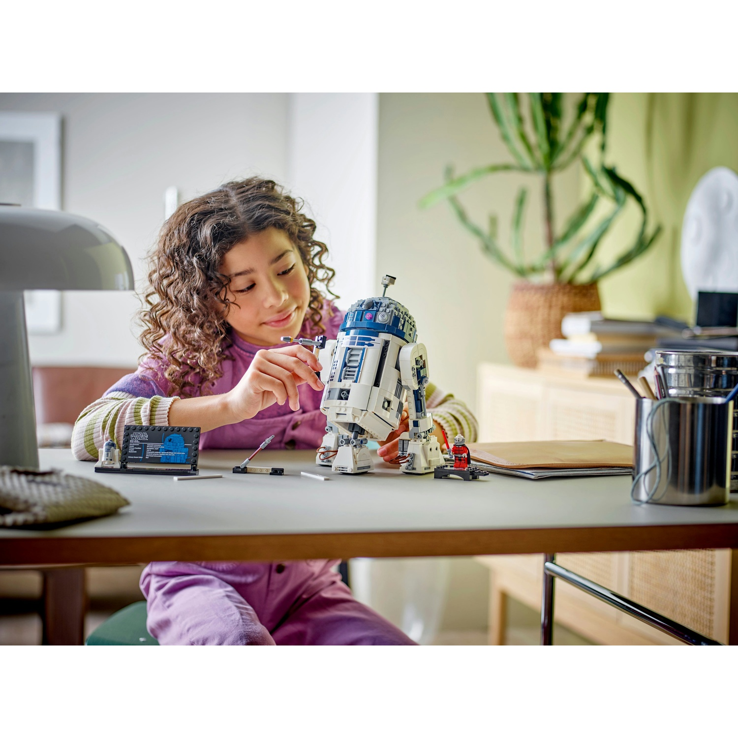 Una ragazza sta assemblando un modello Lego R2-D2. È a una scrivania con istruzioni e strumenti.