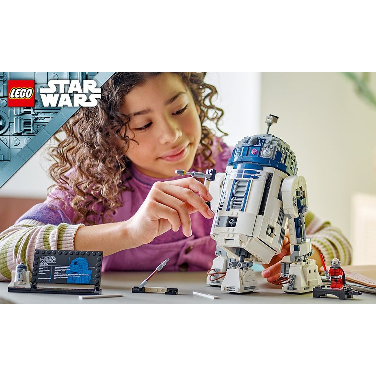Una ragazza gioca con un modello Lego Star Wars R2-D2. Logo Lego Star Wars nell'angolo.
