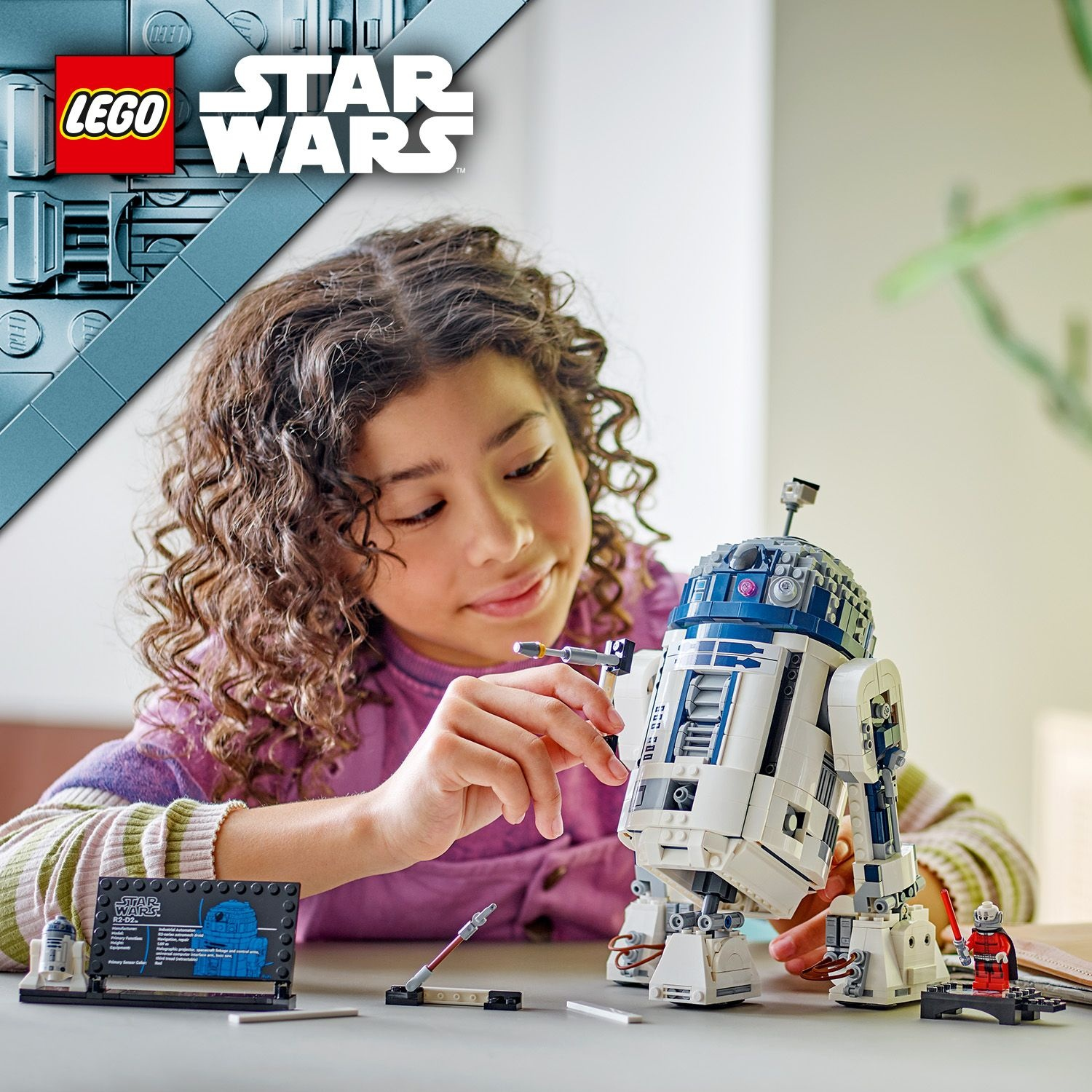 Una ragazza costruisce un modello Lego di R2-D2 di Star Wars, con pezzi Lego e una figura.