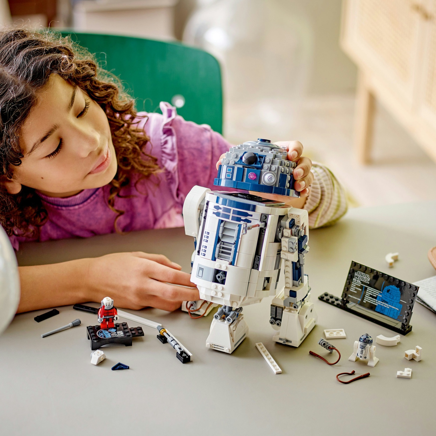 Una ragazza guarda un modello Lego R2-D2, pezzi da costruzione sul tavolo.