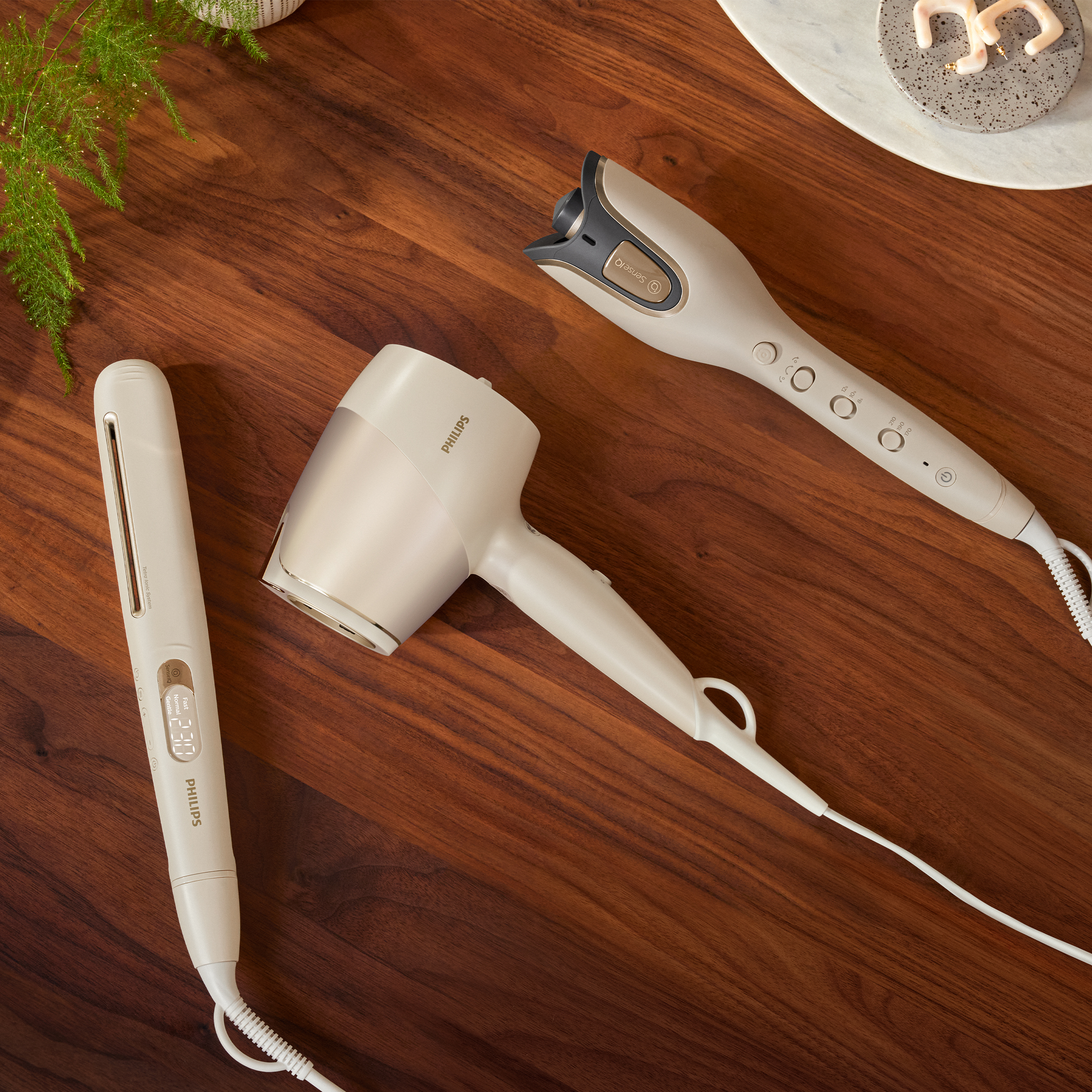 Trzy narzędzia do stylizacji włosów na drewnianej powierzchni: prostownica, suszarka i lokówka.