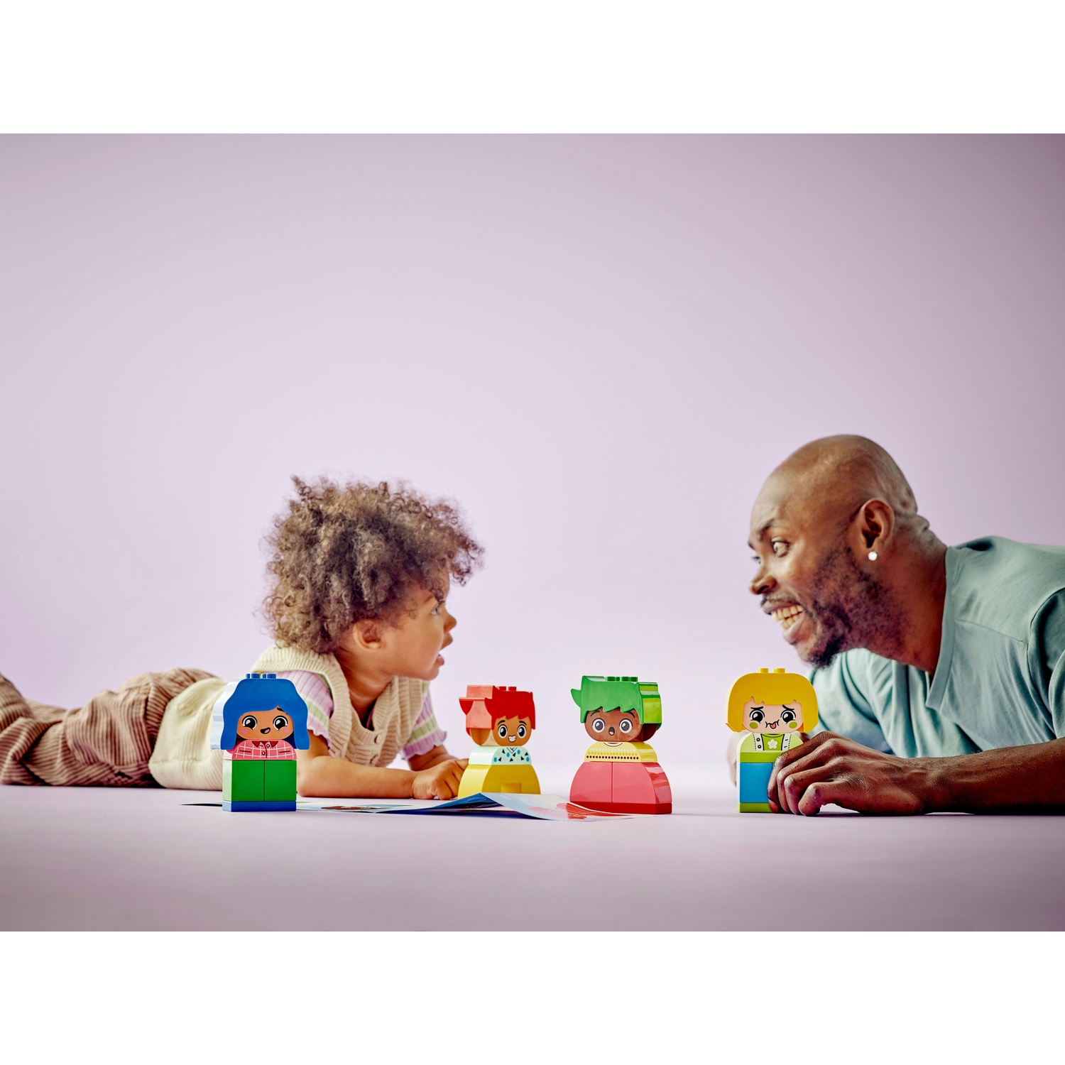 Un padre e un bambino giocano con dei personaggi giocattolo. I giocattoli sono colorati e lo sfondo è rosa.