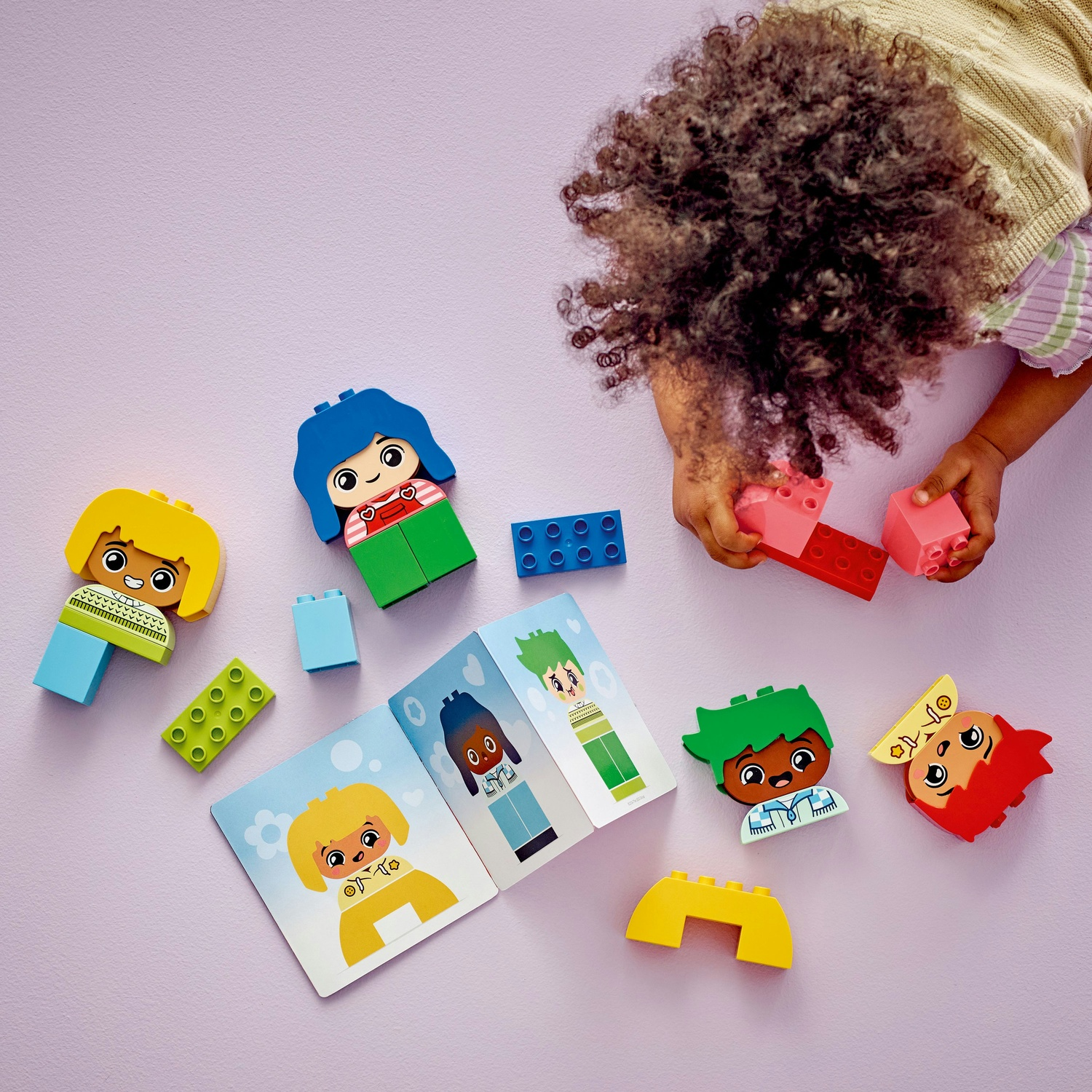 Bambino che gioca con i Lego. Un'auto, delle figure e una baseplate sono visibili.