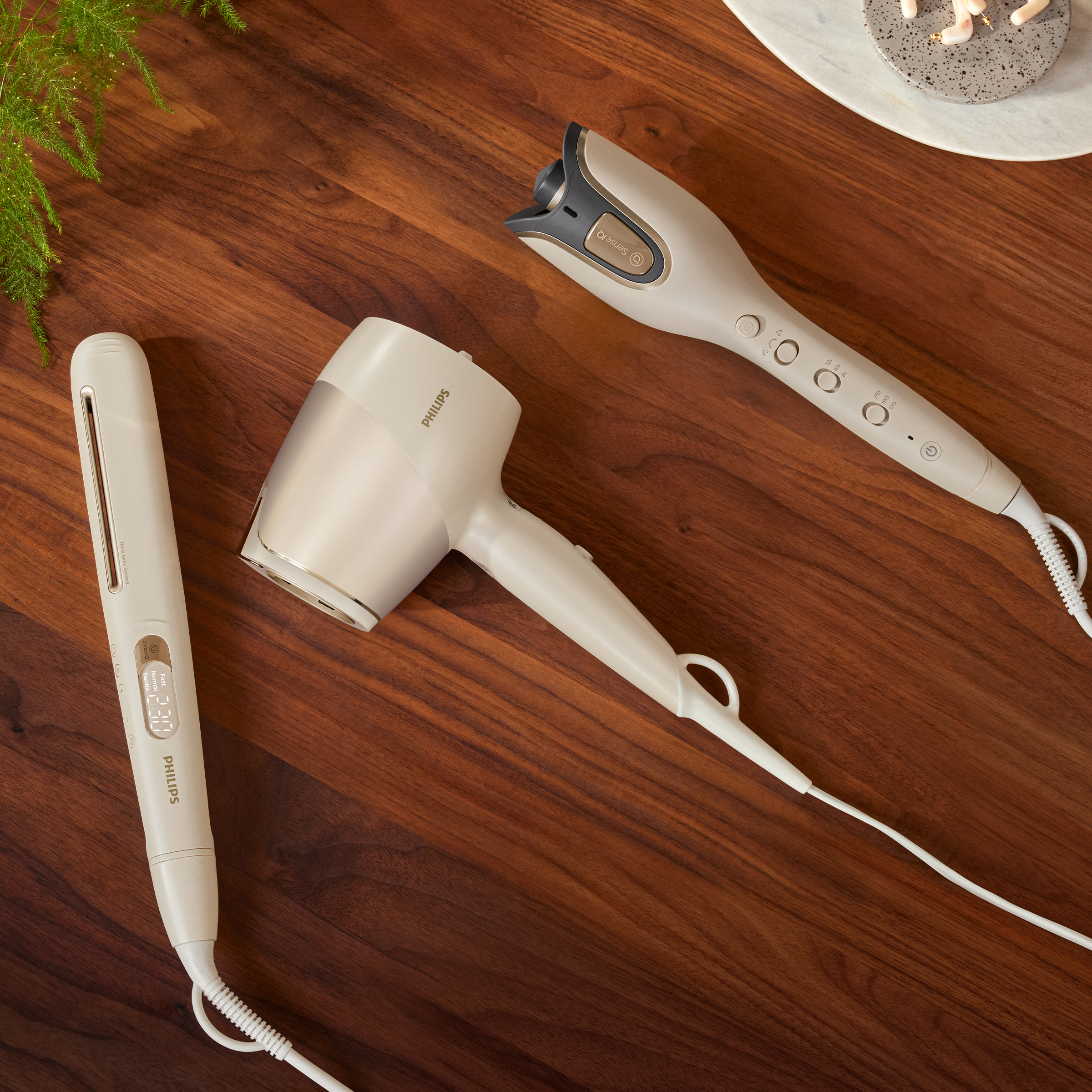 Trzy narzędzia do stylizacji włosów na drewnianej powierzchni: prostownica, suszarka do włosów i lokówka.