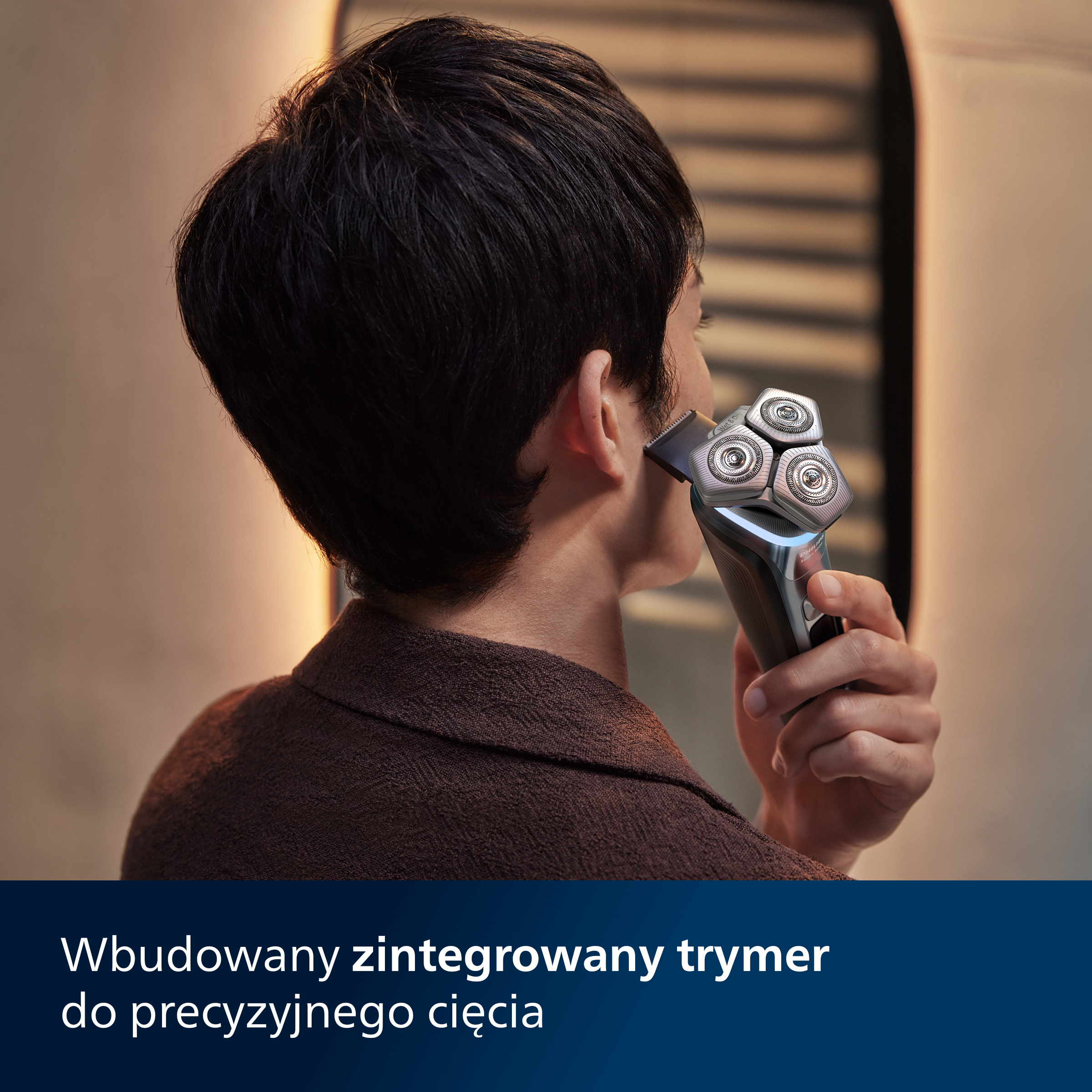 Mężczyzna goli ucho czarno-srebrną golarką elektryczną, w łazience.