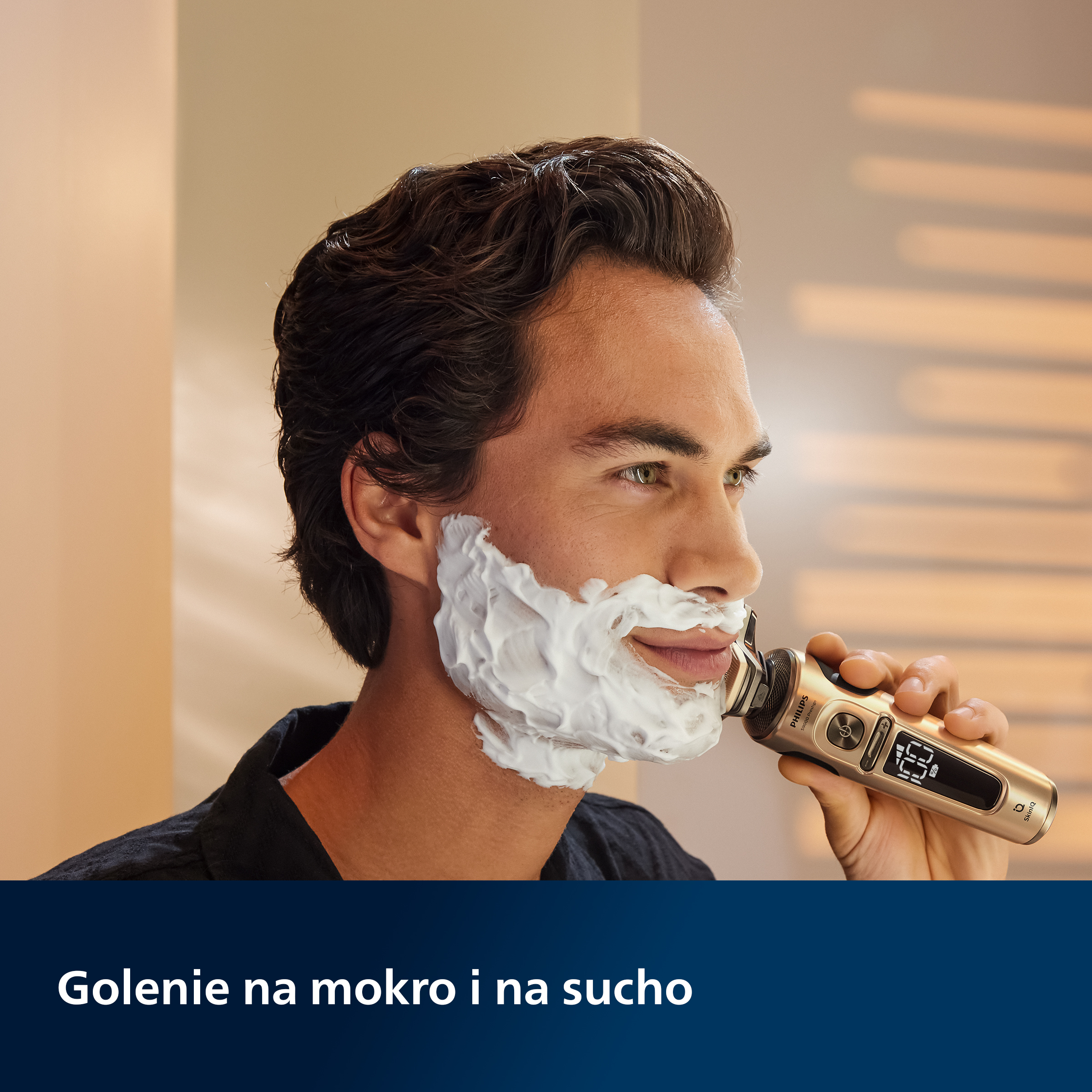 Mężczyzna goli się golarką elektryczną Philips, piana na twarzy. Beżowe tło, uśmiechnięty.