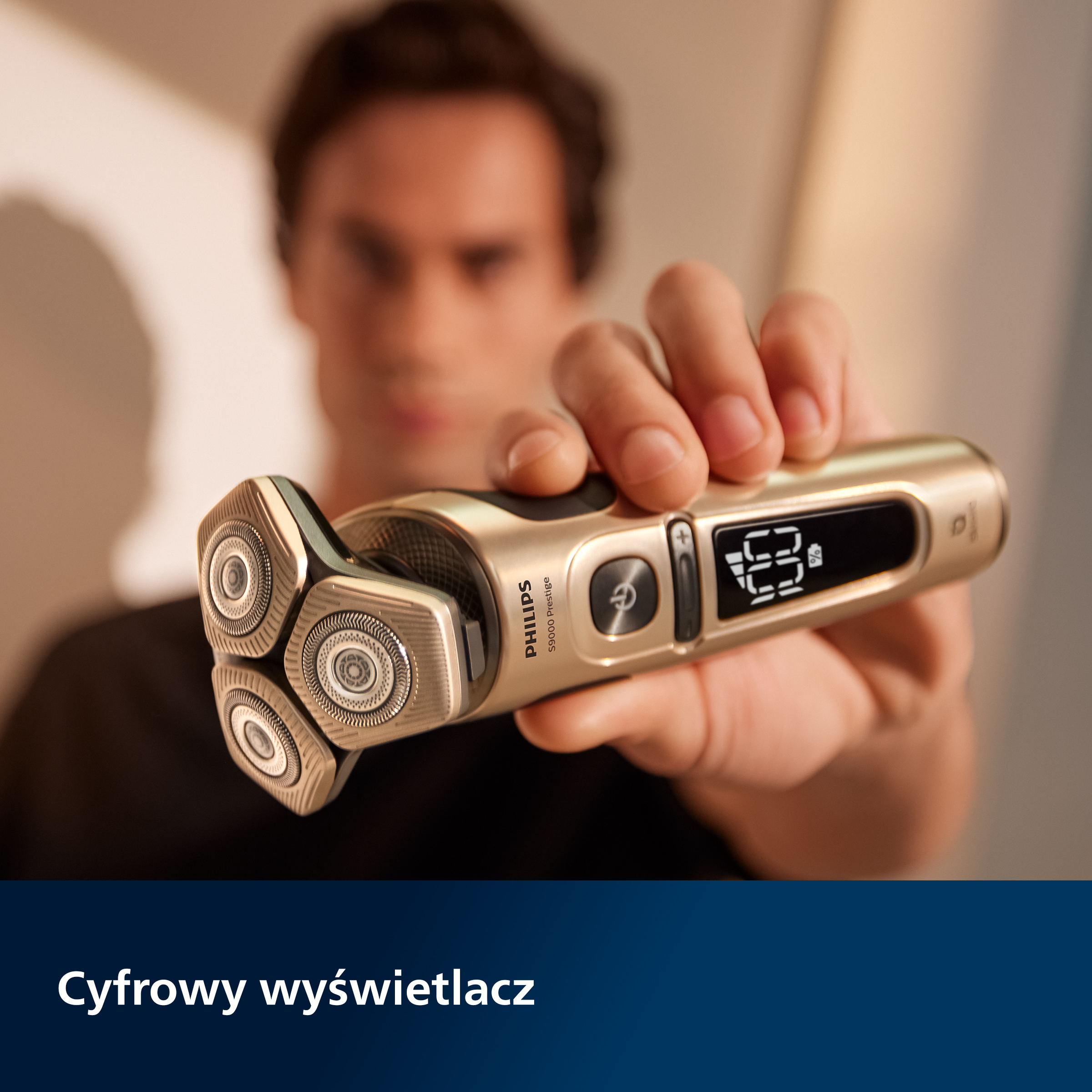 Mężczyzna trzymający złotą i srebrną golarkę elektryczną z cyfrowym wyświetlaczem. Golarka jest ostra.