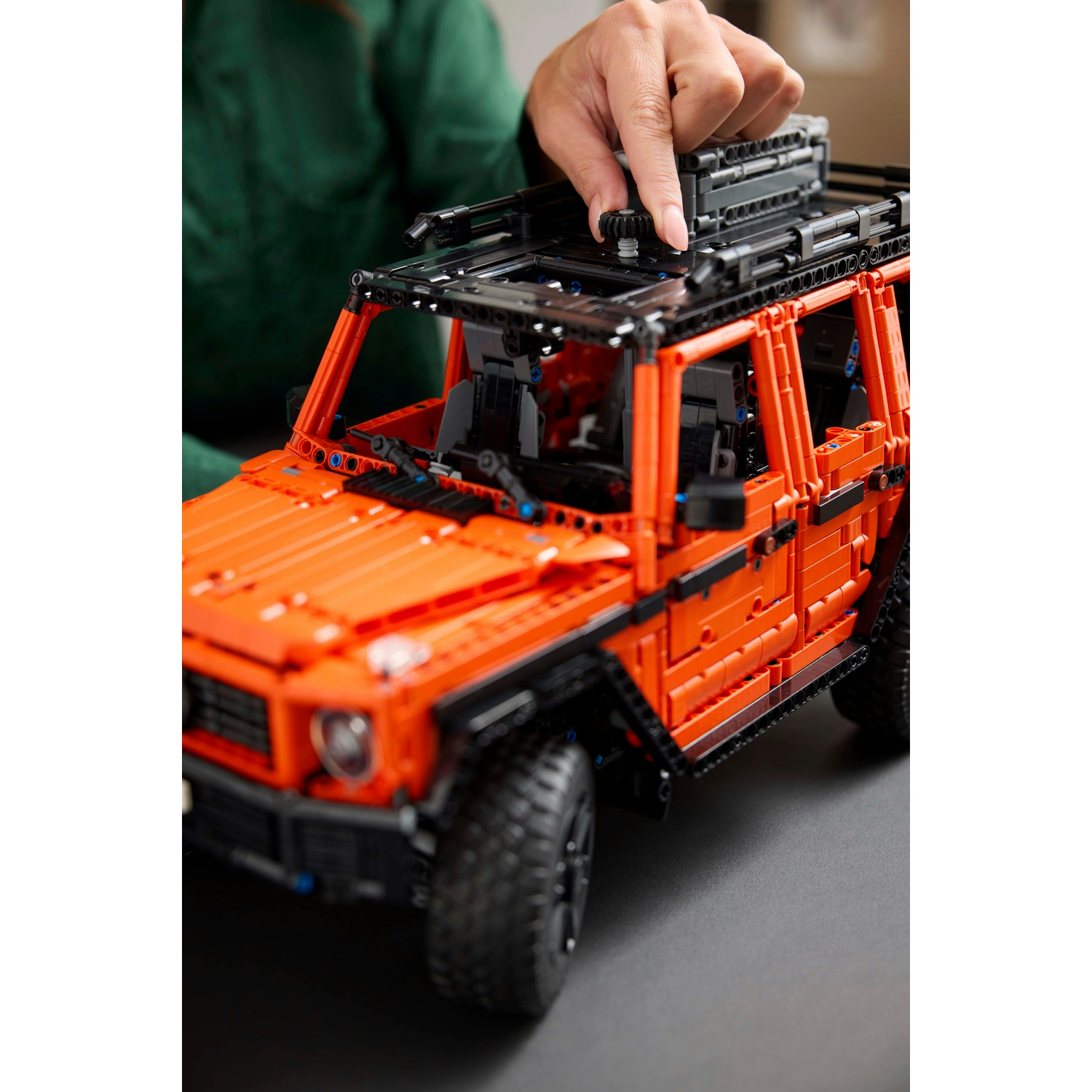 Un modello Lego arancione di un'auto fuoristrada. La mano di una persona è sopra il modello.