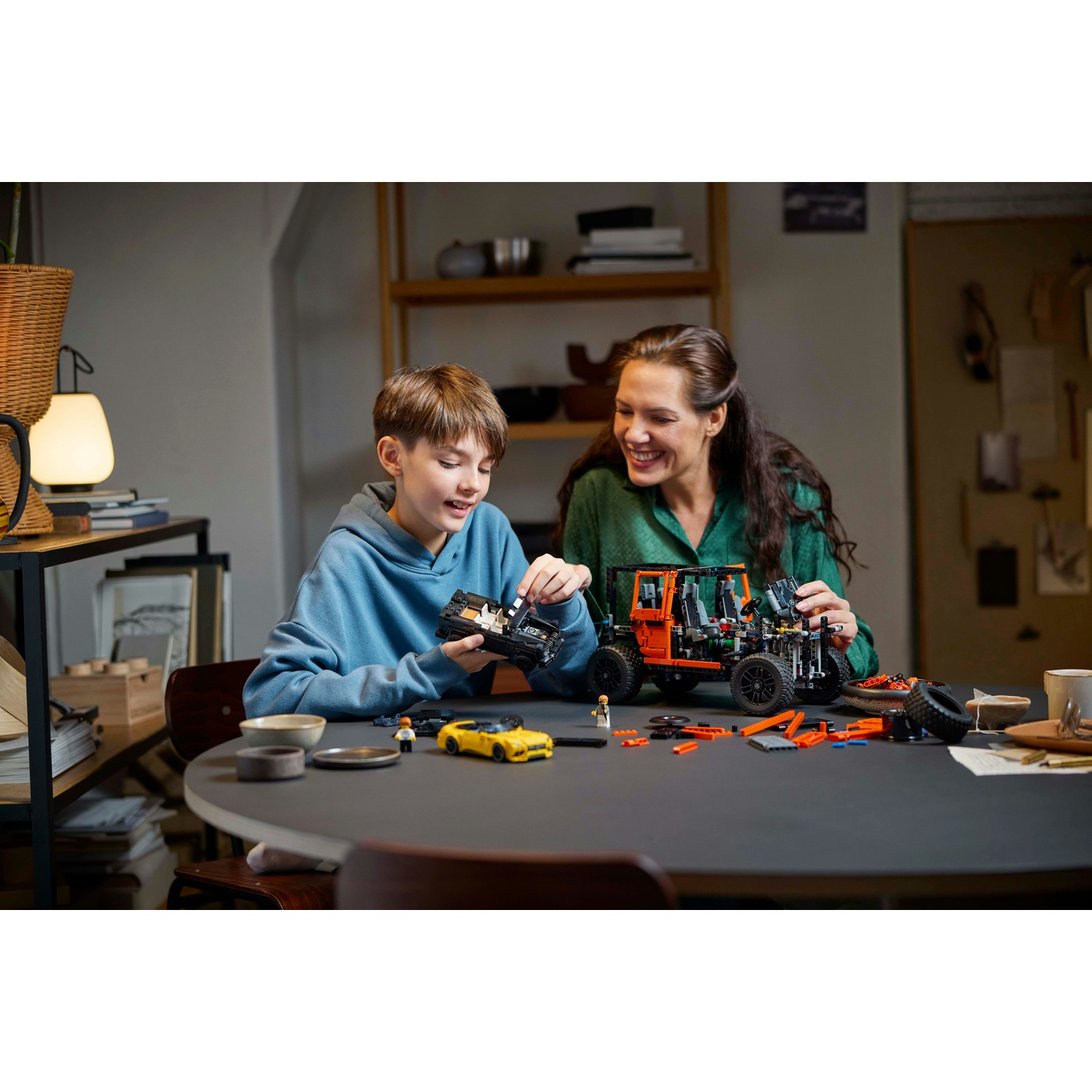 Un ragazzo e una donna che costruiscono un set LEGO Technic. Il tavolo ha pezzi LEGO e un'auto gialla.