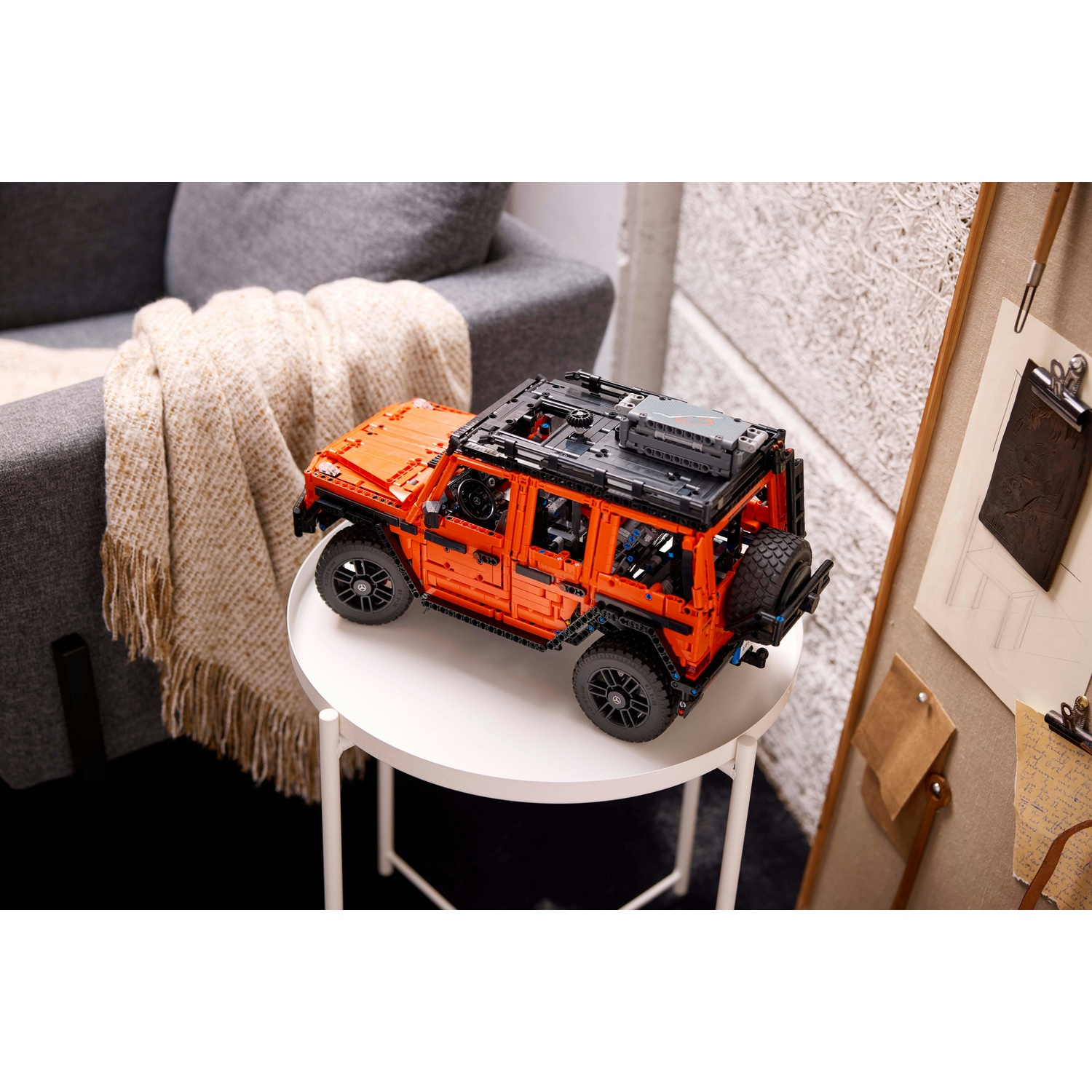 Un modello Lego arancione di un'auto su un tavolo bianco, con un divano e altri oggetti sullo sfondo.