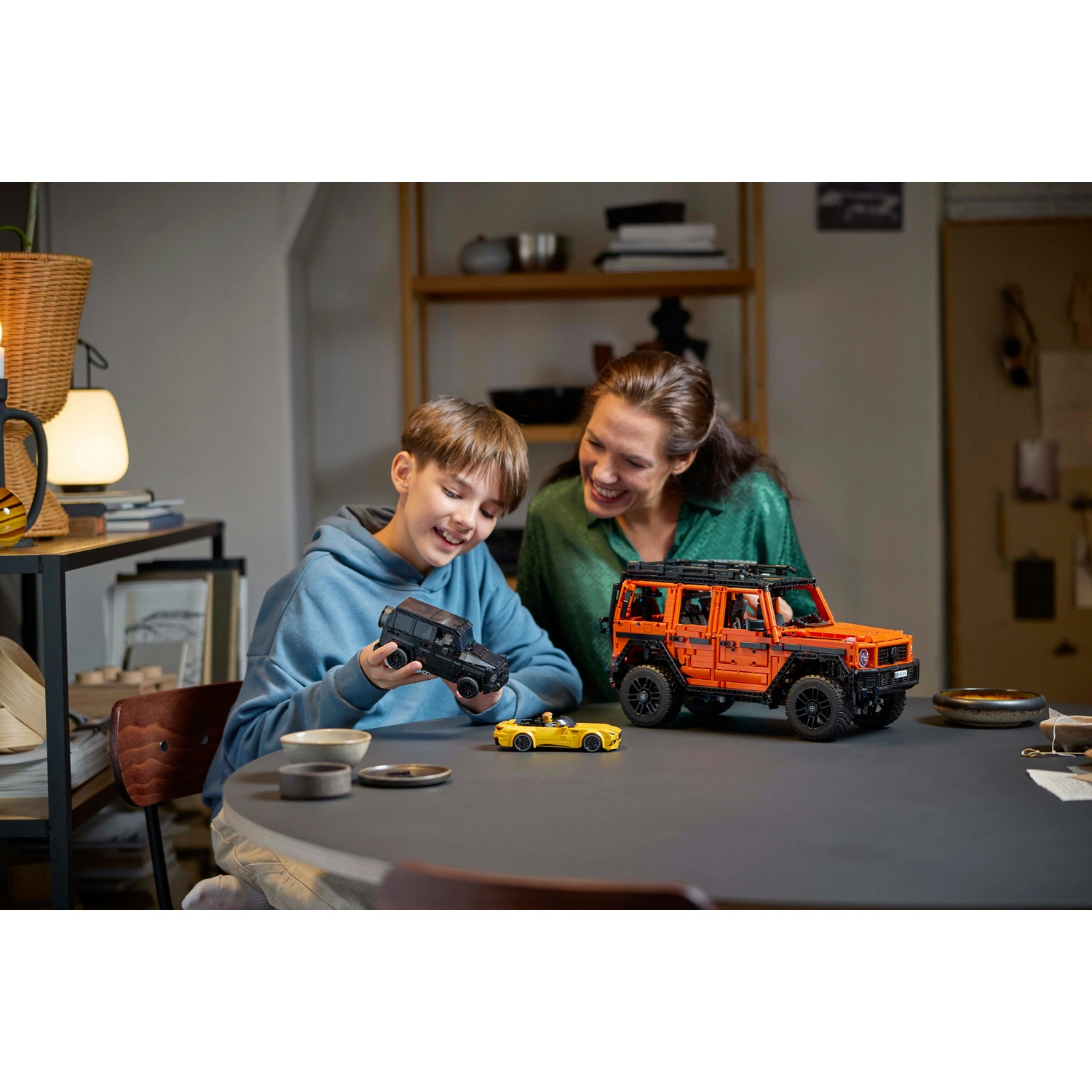 Una madre e un figlio giocano con modelli di auto Lego su un tavolo.