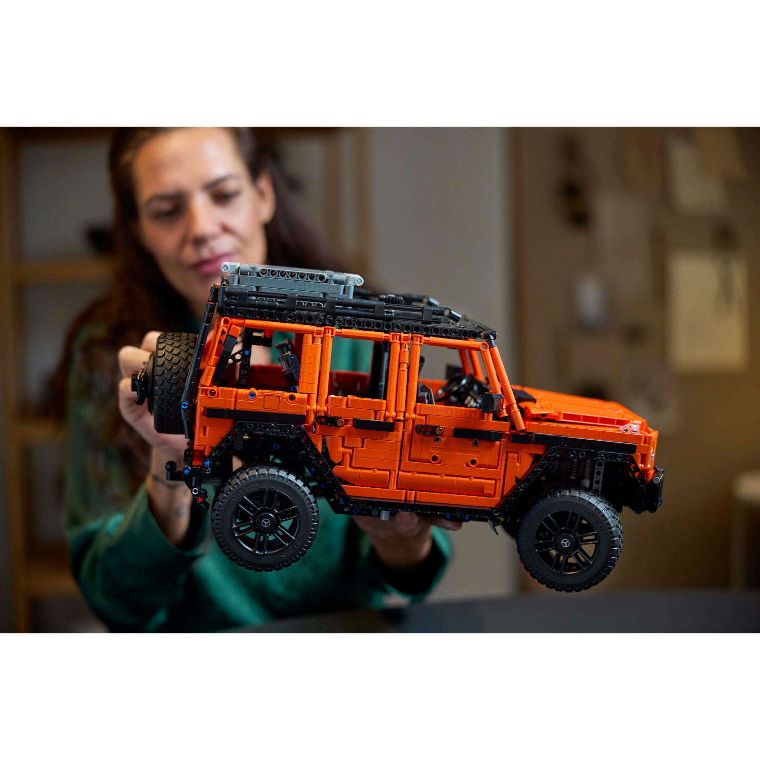 Un'auto Lego arancione, tenuta da una donna. Ha ruote nere.