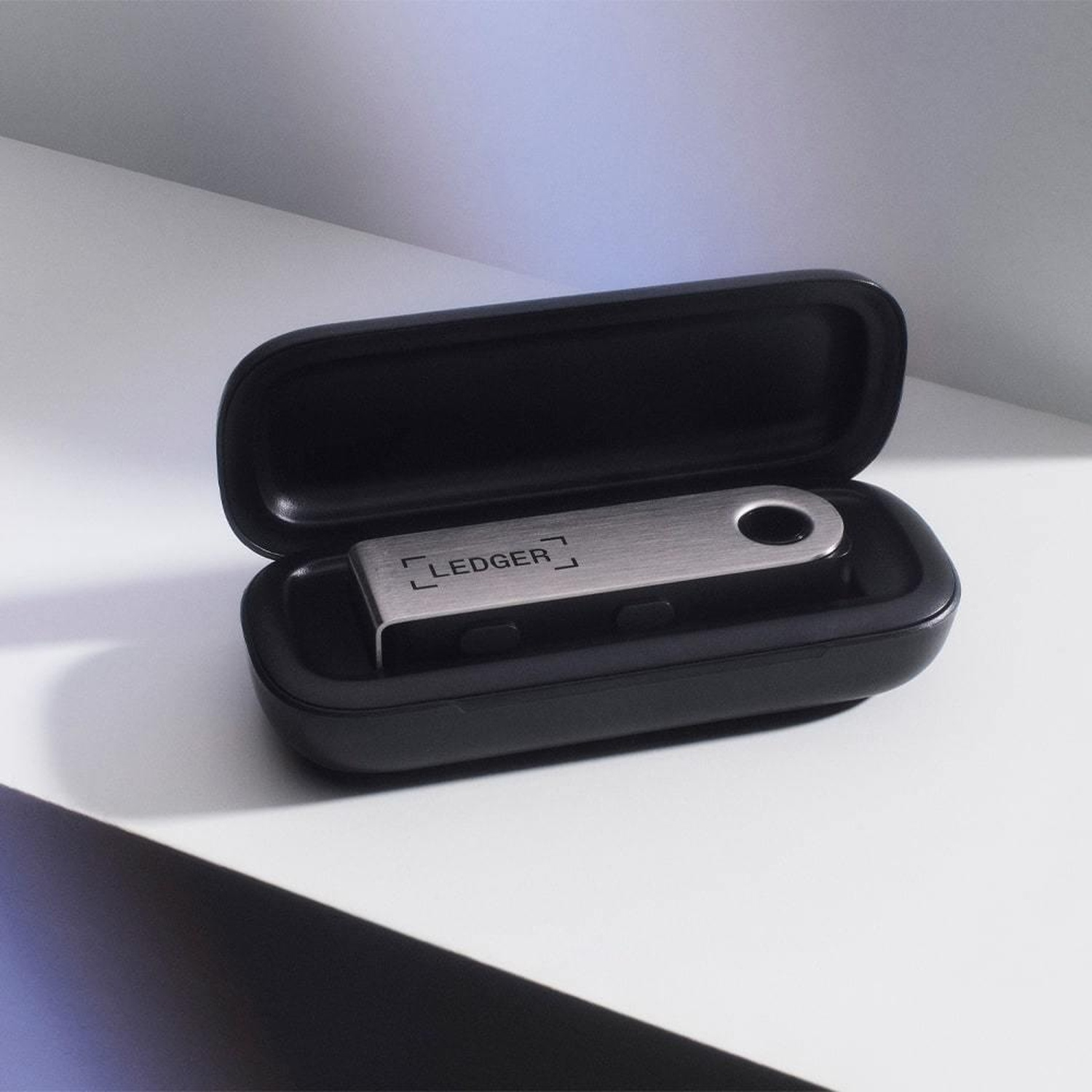 Portafoglio hardware Ledger in una custodia nera. Il portafoglio è argentato e ha il logo Ledger.