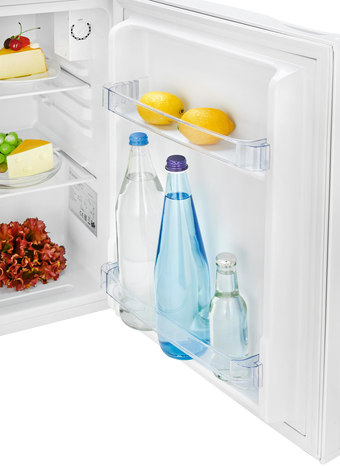 Offener Kühlschrank mit Zitronen, Wasserflaschen, Käsekuchen, Salat und Käse. Weißer Innenraum mit Glasböden.