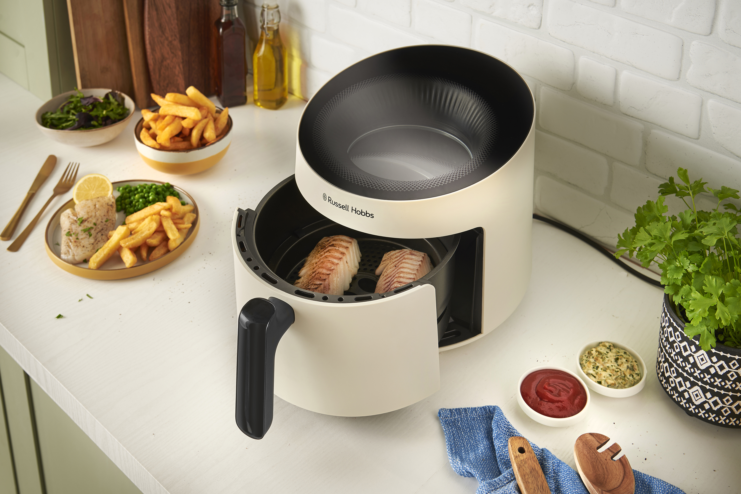 Egy air fryer étellel, egy tányér étellel és mártásokkal egy fehér pulton.