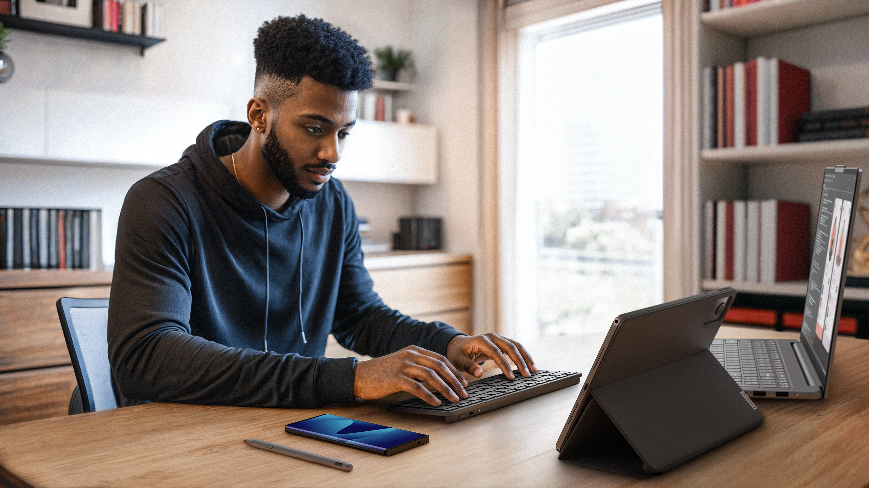 Ein Mann mit dunkler Haut arbeitet an einem Schreibtisch mit Laptop, Tablet und Telefon.
