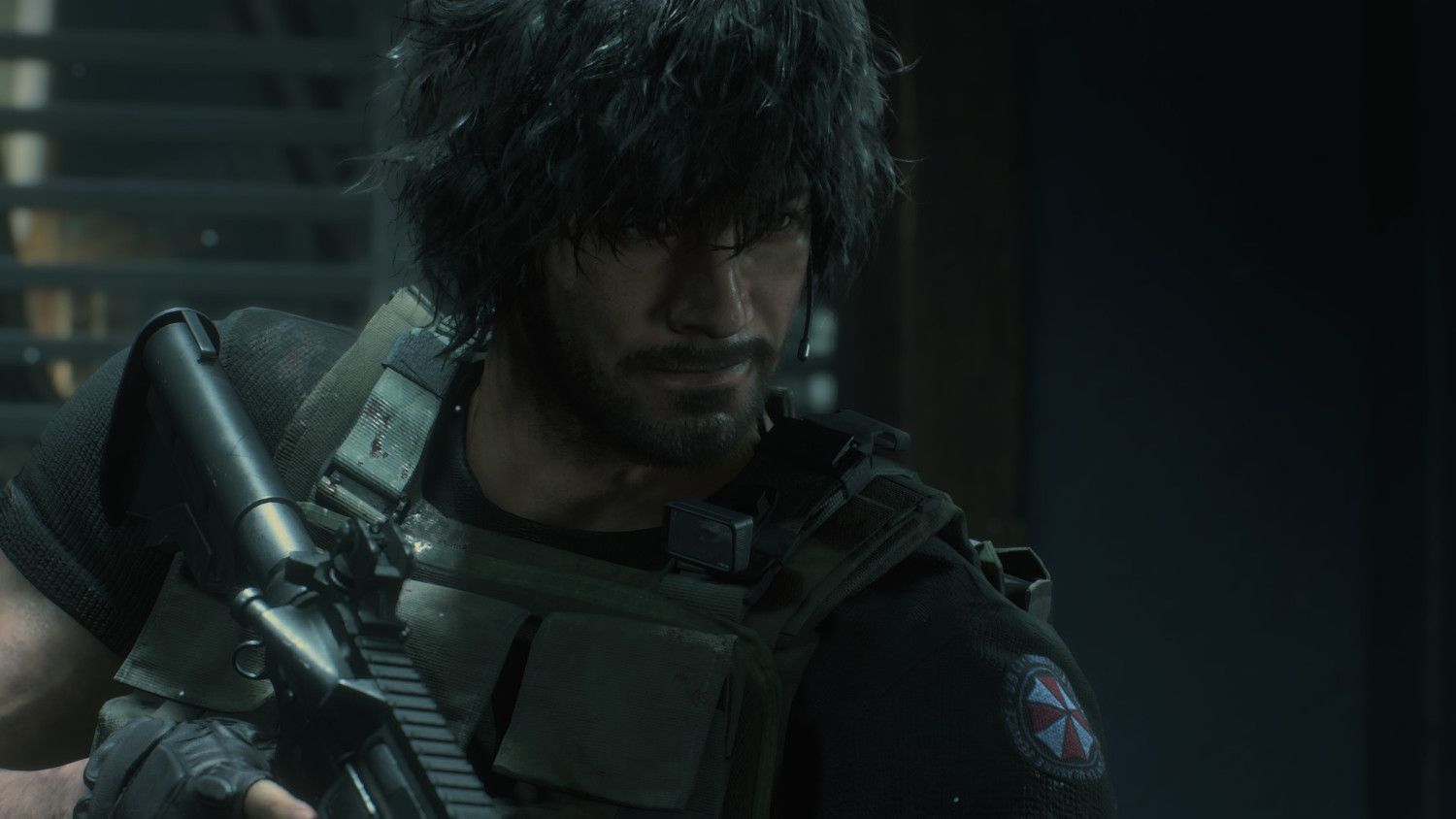 Un homme aux cheveux noirs courts et à la barbe, portant un gilet de combat et tenant une arme, regardant vers la gauche.