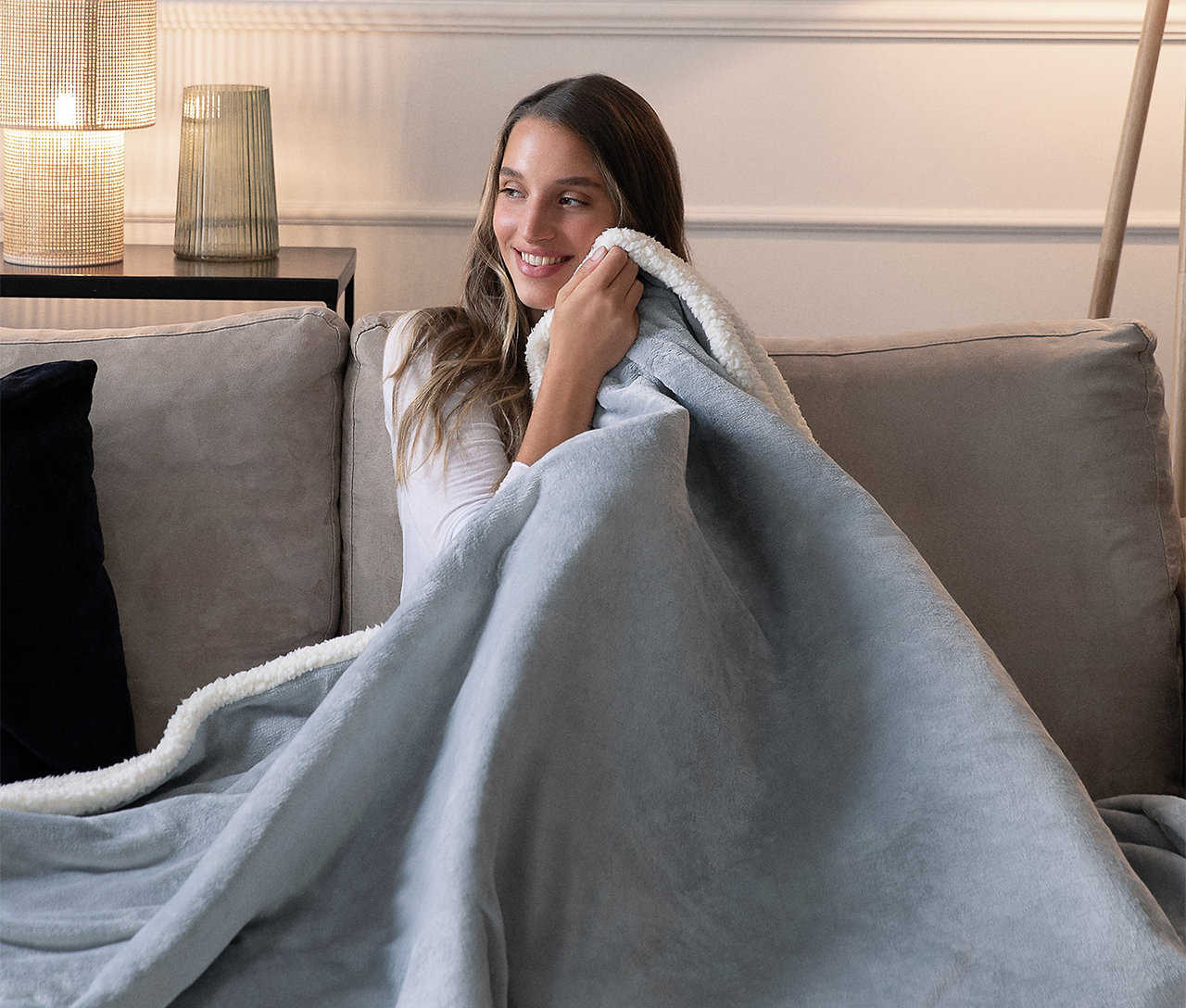 Donna su un divano che tiene una coperta blu, sorridendo.