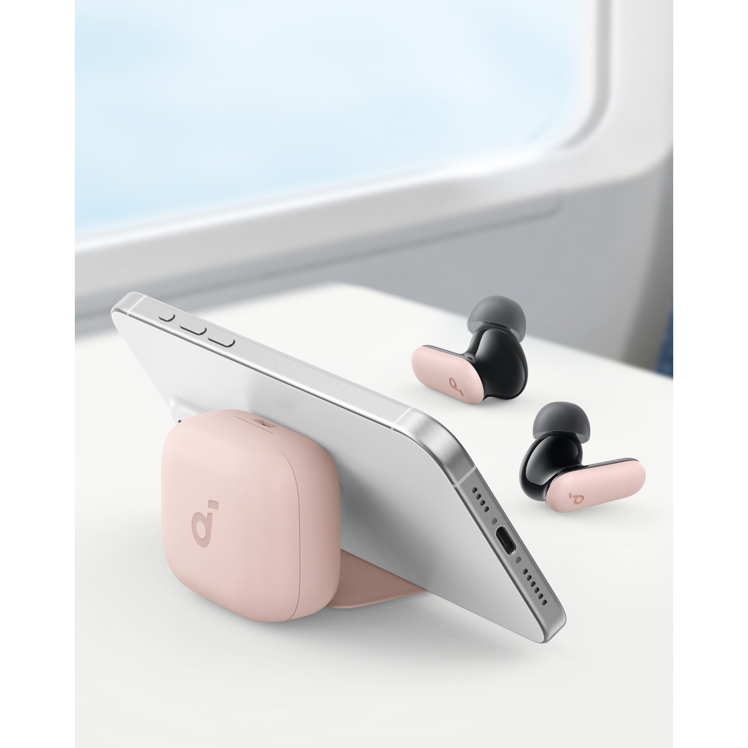 Pink charging station with a phone and black and pink earbuds on a white surface, near a window.
