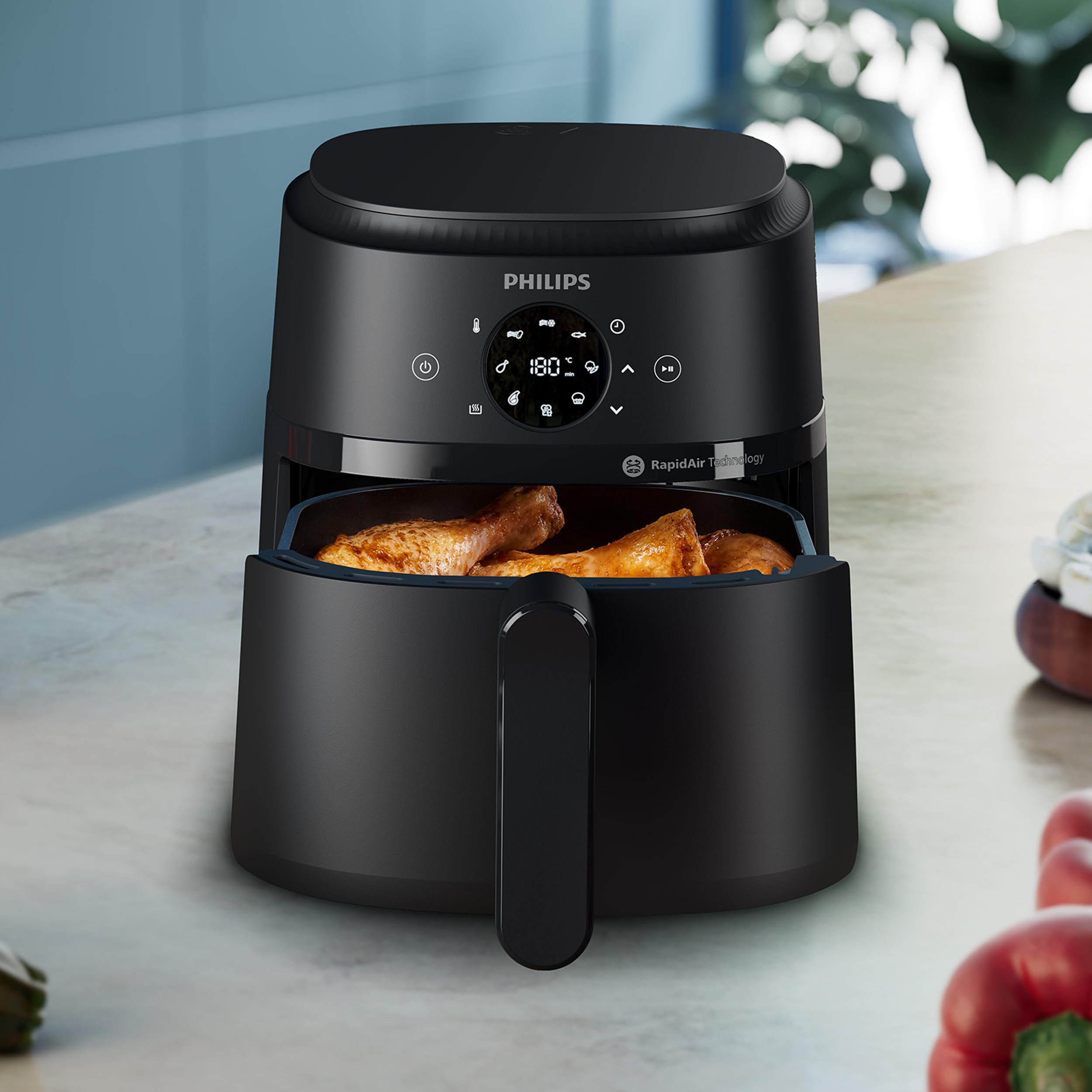 Schwarze Philips Heißluftfritteuse mit goldbraunen Hähnchenschenkeln im Korb auf einer Arbeitsplatte.