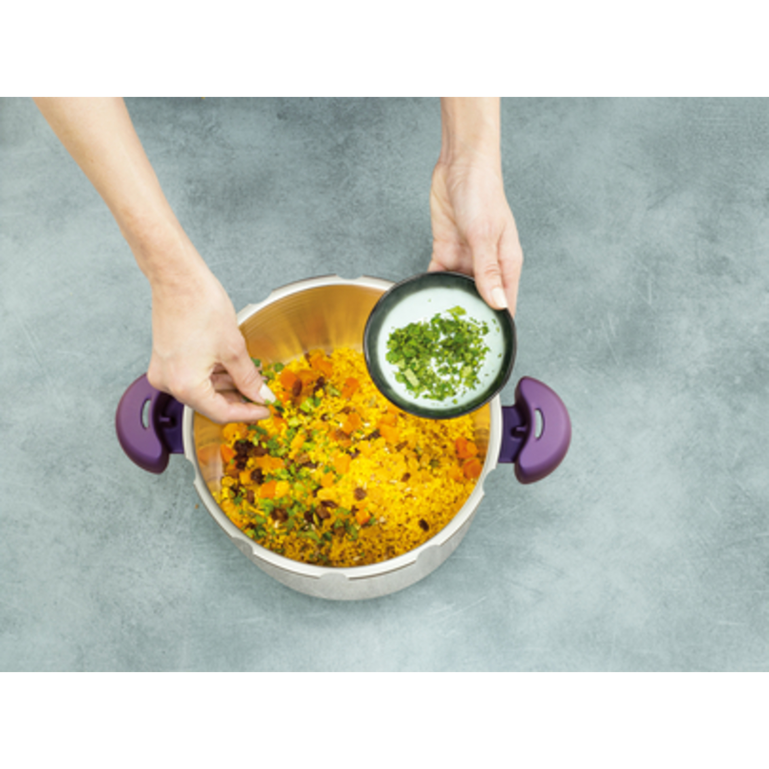 Hands add herbs to a pot of yellow rice with vegetables.