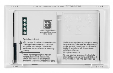 Białe urządzenie, prawdopodobnie czujnik dymu, z instrukcjami i otwartym schowkiem na baterie.