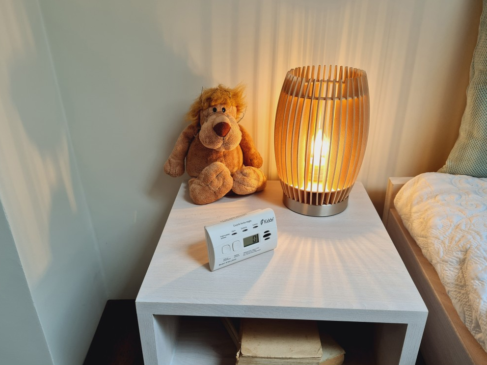 Szafka nocna z lampą, pluszowym lwem i czujnikiem tlenku węgla.